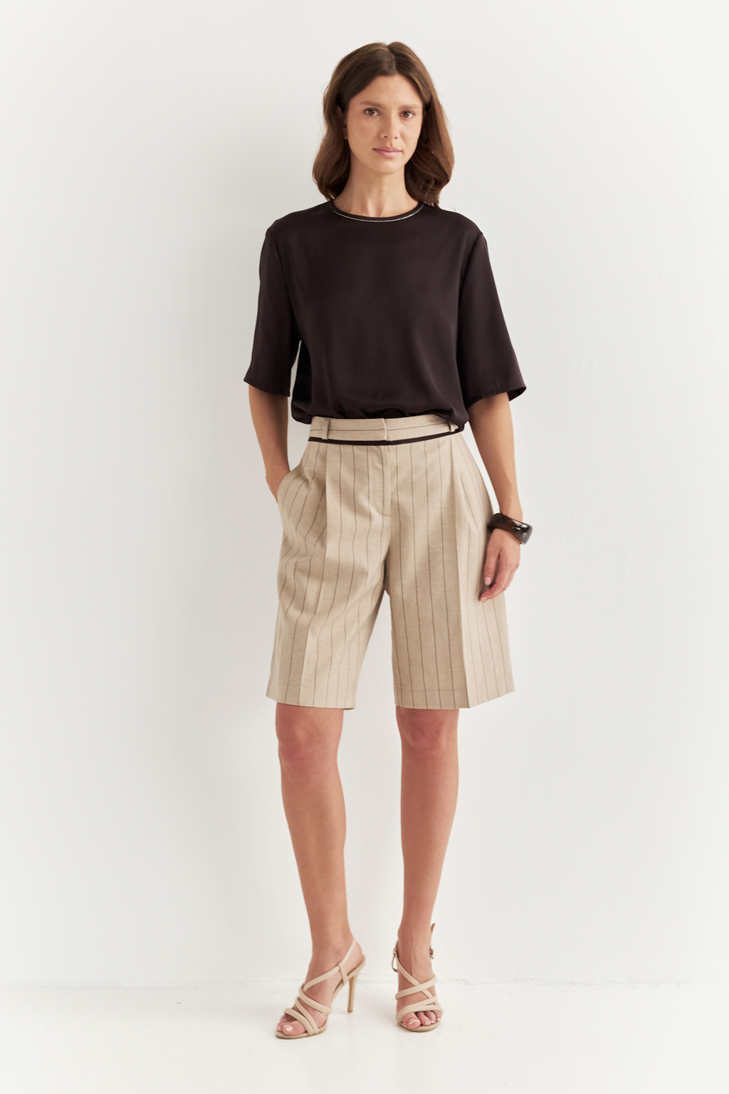 Элегантные шорты из костюмной ткани в полоску с деликатным меланжевым эффектом – безусловный фаворит сезона. Свободный, ниспадающий силуэт подчеркивает непринужденную элегантность и обеспечивает исключительный комфорт. Эти шорты великолепно дополняют жакеты, легкие трикотажные блузы или эффектные топы. Отголоски мужского кроя в дизайне проявляются в классической застежке-гульфике, поясе со шлевками, предусматривающем ношение ремня, и функциональных карманах. Аккуратный кант по линии пояса служит связующим звеном, объединяя шорты и идеально сочетающийся жакет в единый образ.