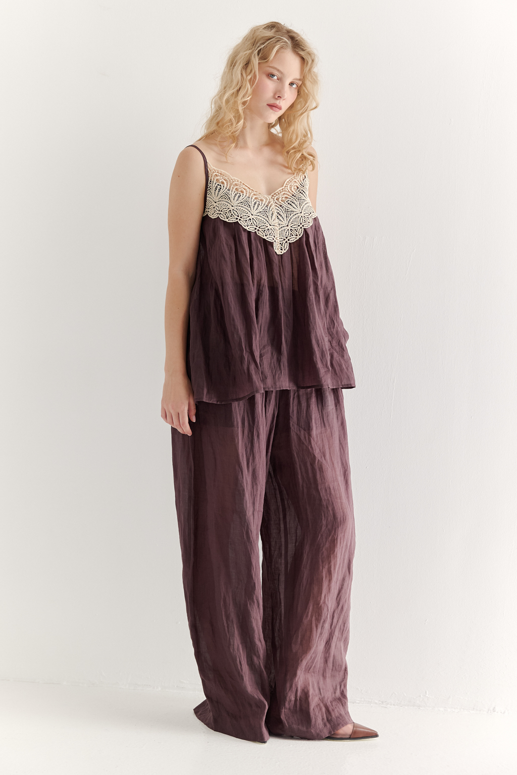 Топ-трапеция, выполненный из стопроцентной крапивы с крэш-эффектом благородного коричневого оттенка, украшен отделкой из кружевного гипюра нежного бежевого цвета. Кружевная деталь изысканно располагается на передней части изделия. Деталь переда топа настрочены на кружево со сборкой, по верхнему срезу спинки предусмотрена резинка, обеспечивающая оптимальную посадку. Бретели топа регулируются. Топ представляет собой идеальный комплект с брюками из крапивы, льна или хлопка, создавая гармоничный и стильный образ