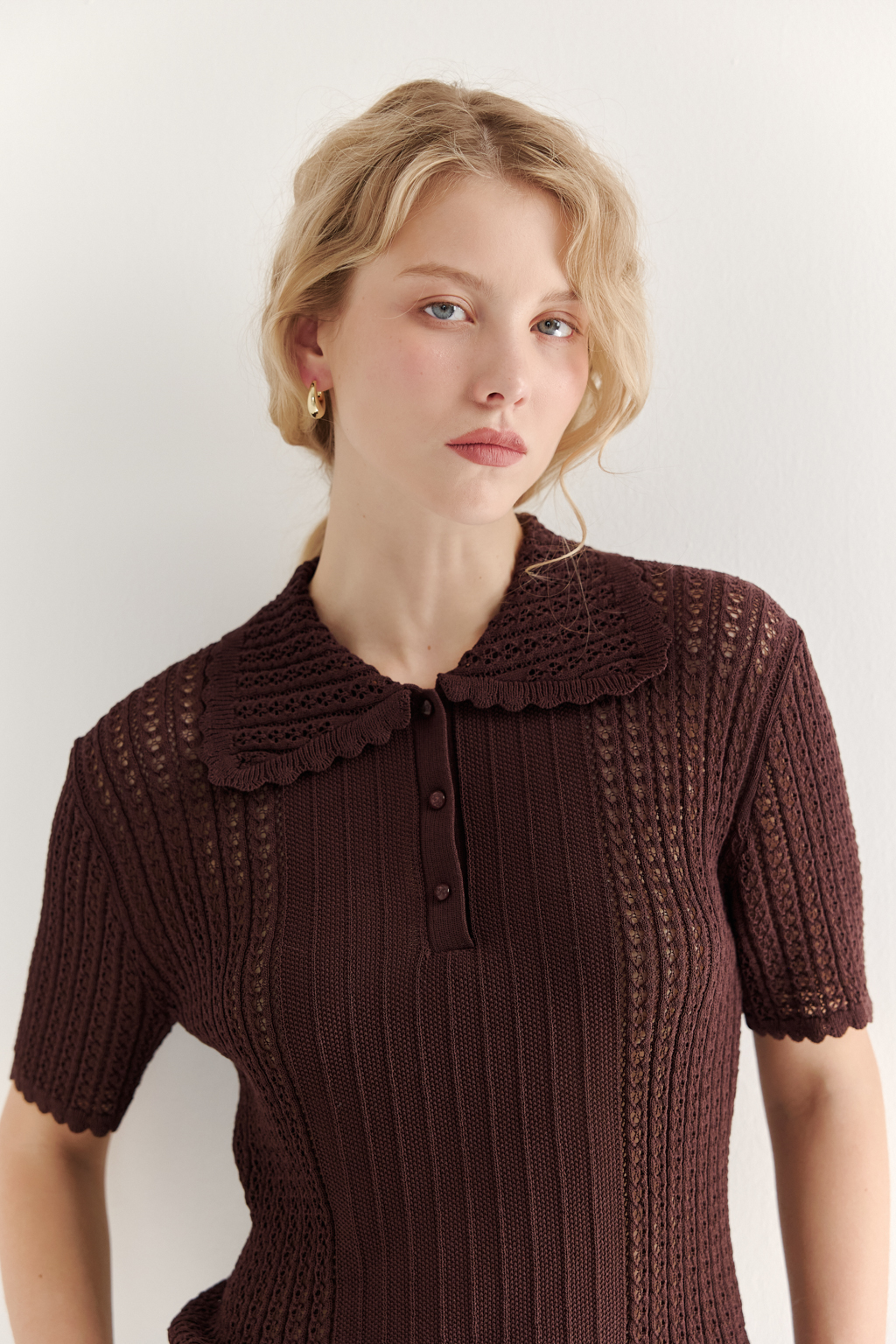 Джемпер-поло шоколадно-коричневого цвета полуприлегающего силуэта средней длины из вискозной пряжи, выполнен в комбинации полупрозрачной сетки и жаккарда, низ рукава и оторочка воротника - изящные фестоны. Рукав короткий, застежка на укороченной планке горловины на три пуговицы.