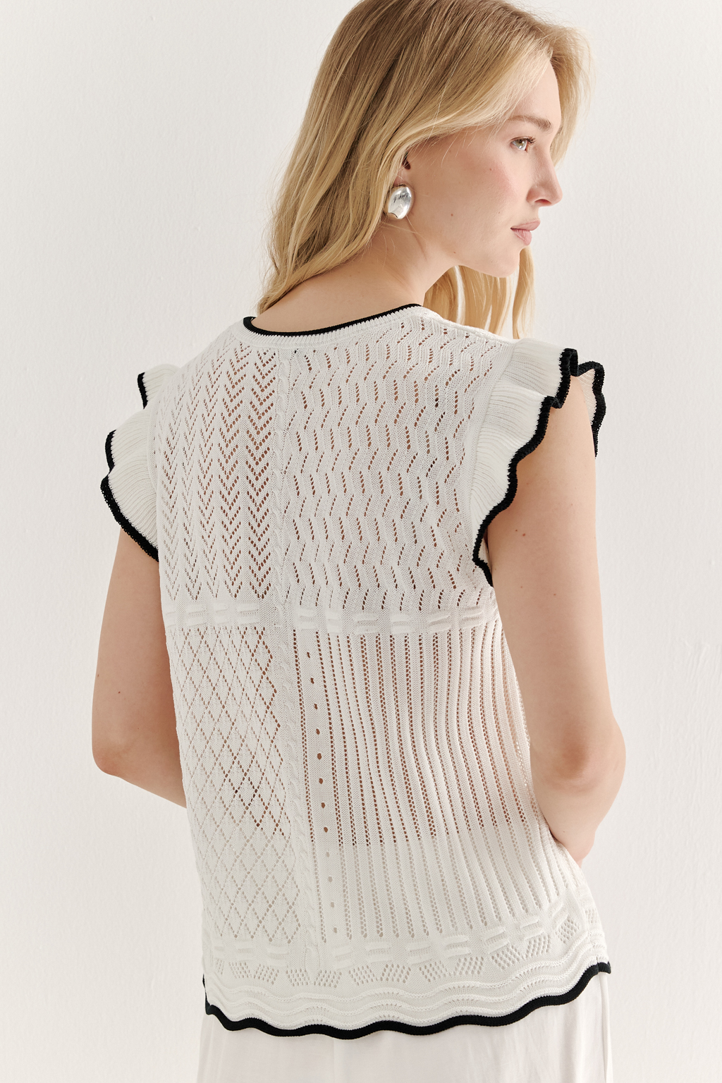 Белый топ, в котором соединились четыре техники ажурной вязки, круглая горловина и деликатные рюши по пройме. Контрастная отделка расположена по линиям горловины, низа и краю рюши.