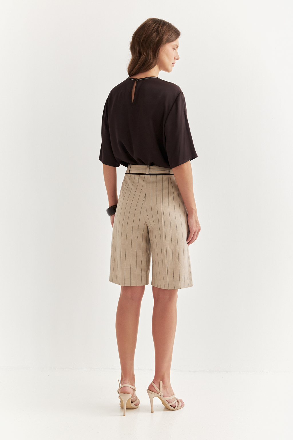 Элегантные шорты из костюмной ткани в полоску с деликатным меланжевым эффектом – безусловный фаворит сезона. Свободный, ниспадающий силуэт подчеркивает непринужденную элегантность и обеспечивает исключительный комфорт. Эти шорты великолепно дополняют жакеты, легкие трикотажные блузы или эффектные топы. Отголоски мужского кроя в дизайне проявляются в классической застежке-гульфике, поясе со шлевками, предусматривающем ношение ремня, и функциональных карманах. Аккуратный кант по линии пояса служит связующим звеном, объединяя шорты и идеально сочетающийся жакет в единый образ.