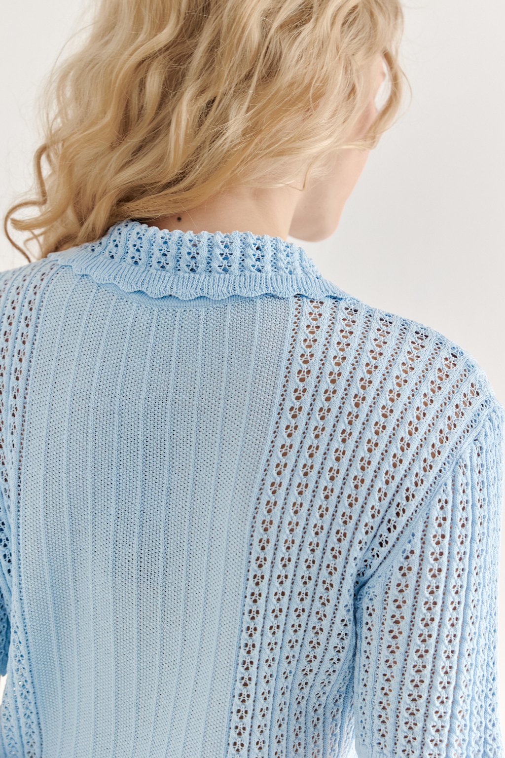 Джемпер-поло нежно-голубого цвета полуприлегающего силуэта средней длины из вискозной пряжи, выполнен в комбинации полупрозрачной сетки и жаккарда, низ рукава и оторочка воротника - изящные фестоны. Рукав короткий, застежка на укороченной планке горловины на три пуговицы.