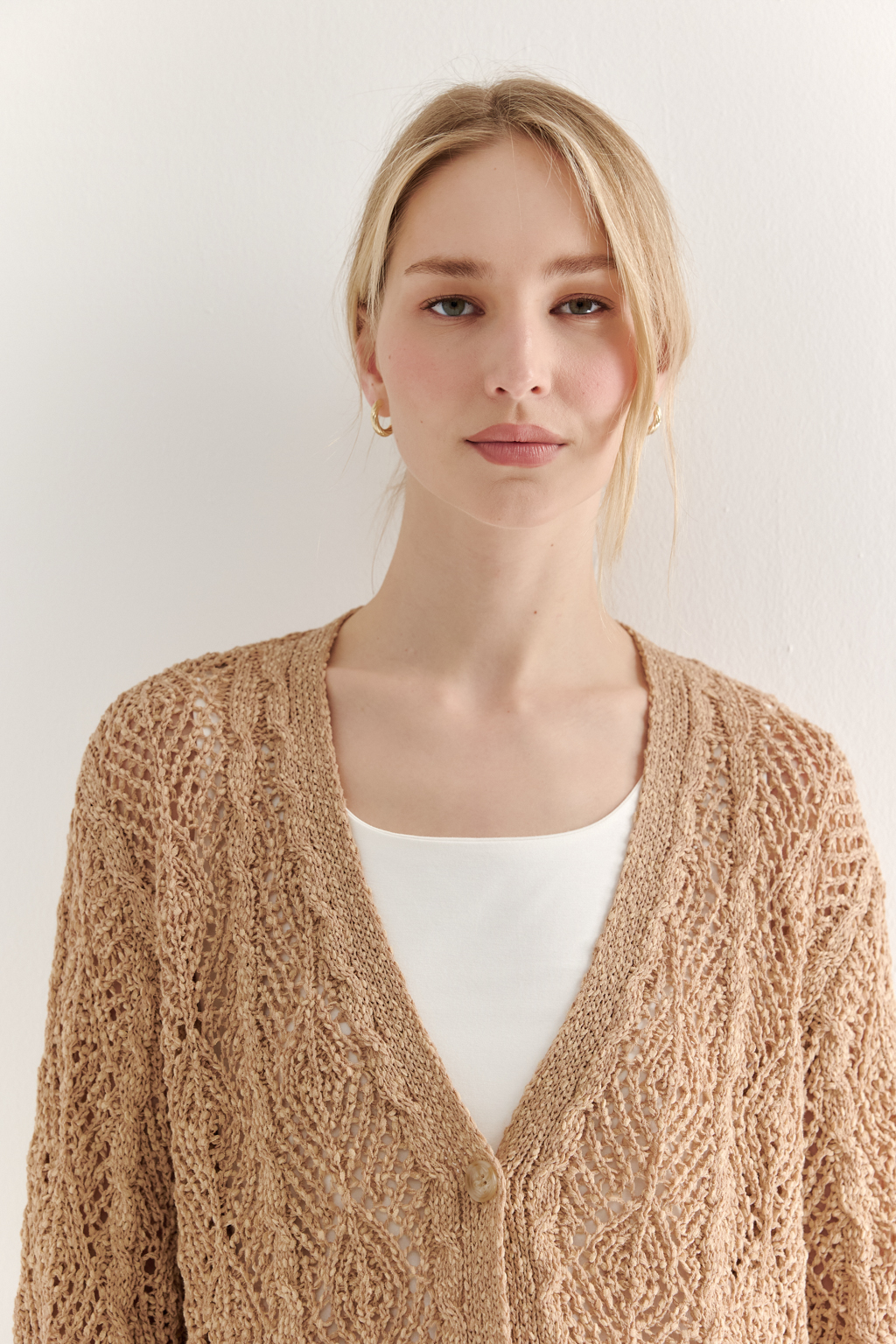 Бежевый вязаный кардиган оверсайз силуэта из хлопковой пряжи. Кардиган связан в сложной технике комбинирования сетки и ажурных ромбов. Рукав прямой удлиненный, V-образный вырез, борт отделан планкой, застежка по борту на 3 пуговицы, низ кардигана и рукав – сложные фестоны.