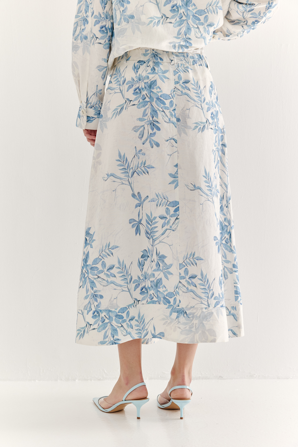 Юбка А-силуэта выполнена из ткани, в составе которой лен и вискоза. Классические детали, такие как пояс, шлевки, гульфик, кокетка спинки и отстроченные швы, представляют собой традиционное решение для джинсовых коллекций. Изюминкой модели является глубокая складка по переднему шву, обеспечивающая дополнительный комфорт и свободу движений. Главный акцент – принт в стиле знаменитого одноцветного Туаль де Жуи, где диагональная композиция из листьев и цветов выполнена в голубом цвете.