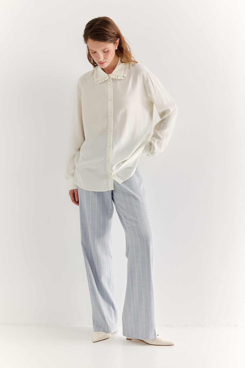 Блуза-батник в нежном оттенке сливочное масло станет изысканным дополнением к жакету, брюкам или верхней одежде, позволяя создавать актуальные многослойные образы. Изготовленная из вискозной ткани, она обладает превосходными тактильными качествами и напоминает дорогой шелковый креп. Классическая блузка свободного кроя с отложным воротником и стойкой, украшенной узким рюшем, имеет планку для застежки и втачной прямой рукав с манжетой на пуговицах.
