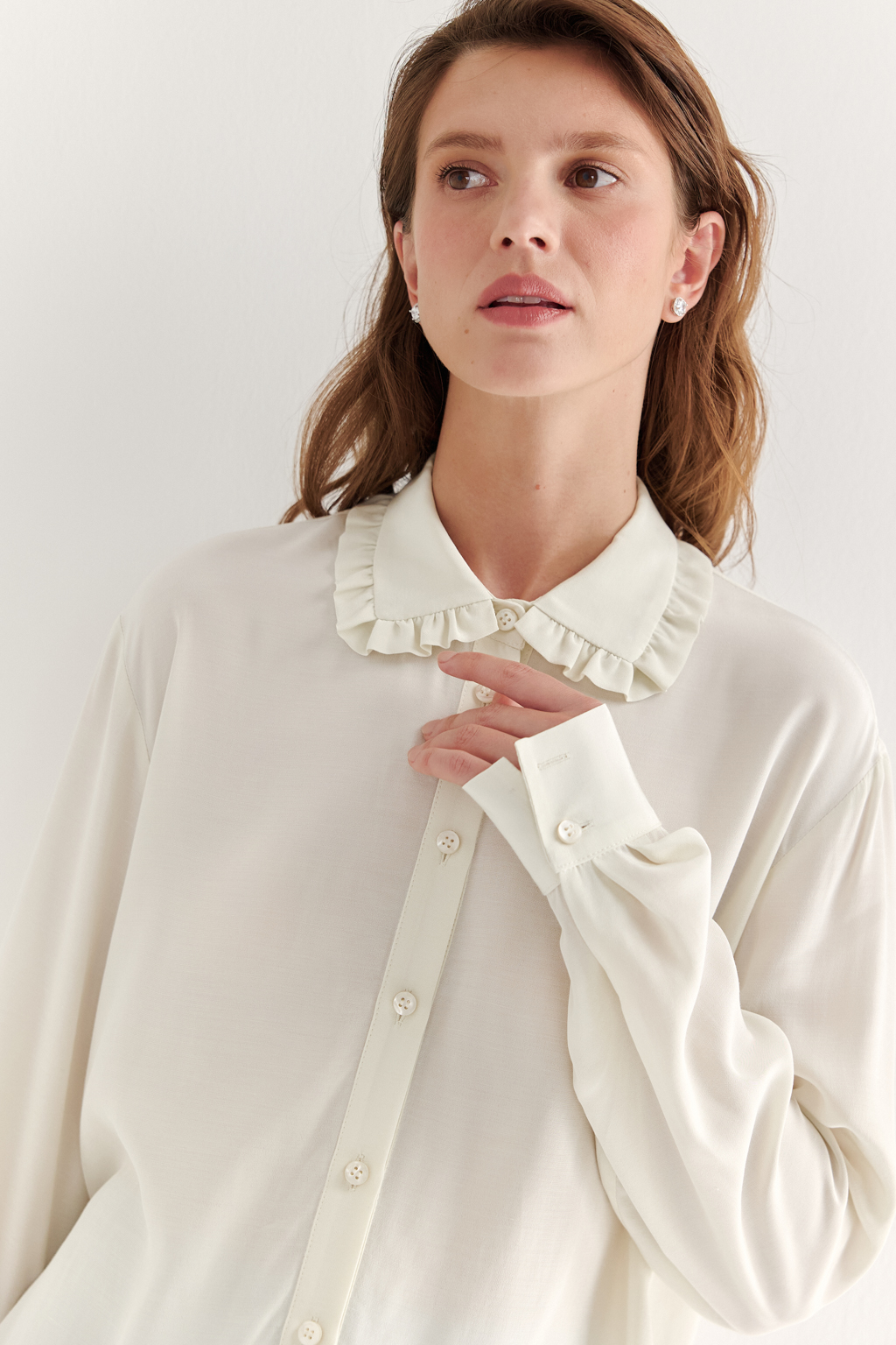 Блуза-батник в нежном оттенке сливочное масло станет изысканным дополнением к жакету, брюкам или верхней одежде, позволяя создавать актуальные многослойные образы. Изготовленная из вискозной ткани, она обладает превосходными тактильными качествами и напоминает дорогой шелковый креп. Классическая блузка свободного кроя с отложным воротником и стойкой, украшенной узким рюшем, имеет планку для застежки и втачной прямой рукав с манжетой на пуговицах.