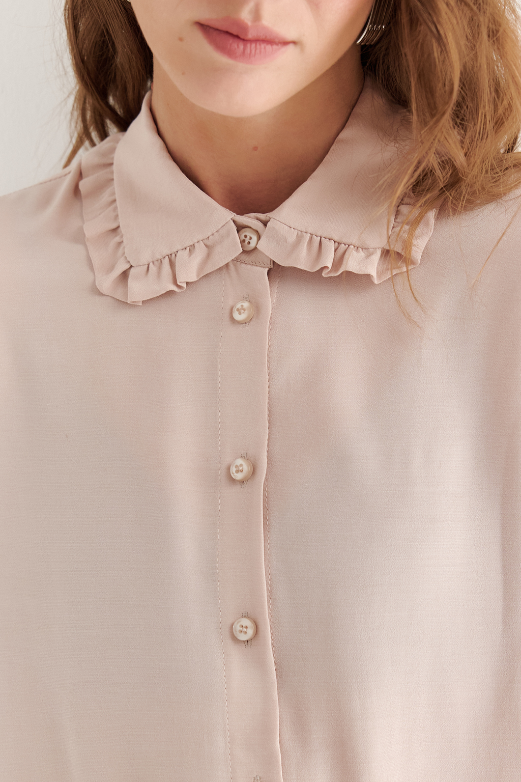 Блуза-батник в нежном пудрово-розовом оттенке станет изысканным дополнением к жакету, брюкам или верхней одежде, позволяя создавать актуальные многослойные образы. Изготовленная из вискозной ткани, она обладает превосходными тактильными качествами и напоминает дорогой шелковый креп. Классическая блузка свободного кроя с отложным воротником и стойкой, украшенной узким рюшем, имеет кокетку спинки, планку для застежки и втачной прямой рукав с манжетой на пуговицах.