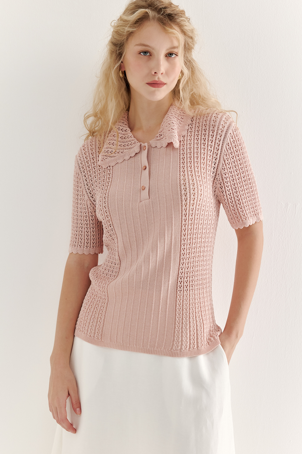 Джемпер-поло нежно-розового цвета полуприлегающего силуэта средней длины из вискозной пряжи, выполнен в комбинации полупрозрачной сетки и жаккарда, низ рукава и оторочка воротника - изящные фестоны. Рукав короткий, застежка на укороченной планке горловины на три пуговицы.