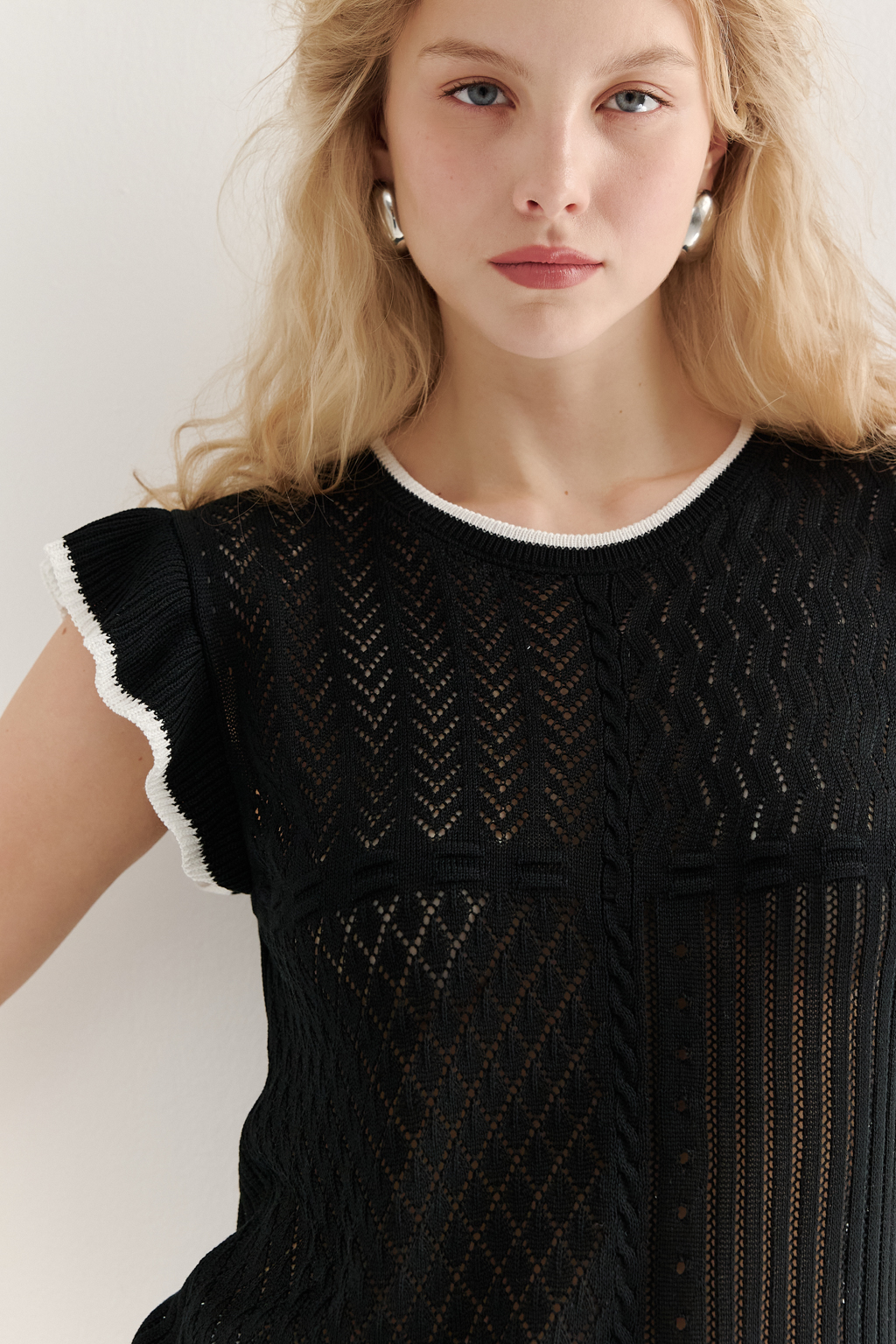 Черный топ в стиле пэчворк, в котором соединились четыре техники ажурной вязки, круглая горловина и деликатные рюши по пройме. Контрастная отделка расположена по линиям горловины, низа и краю рюши.