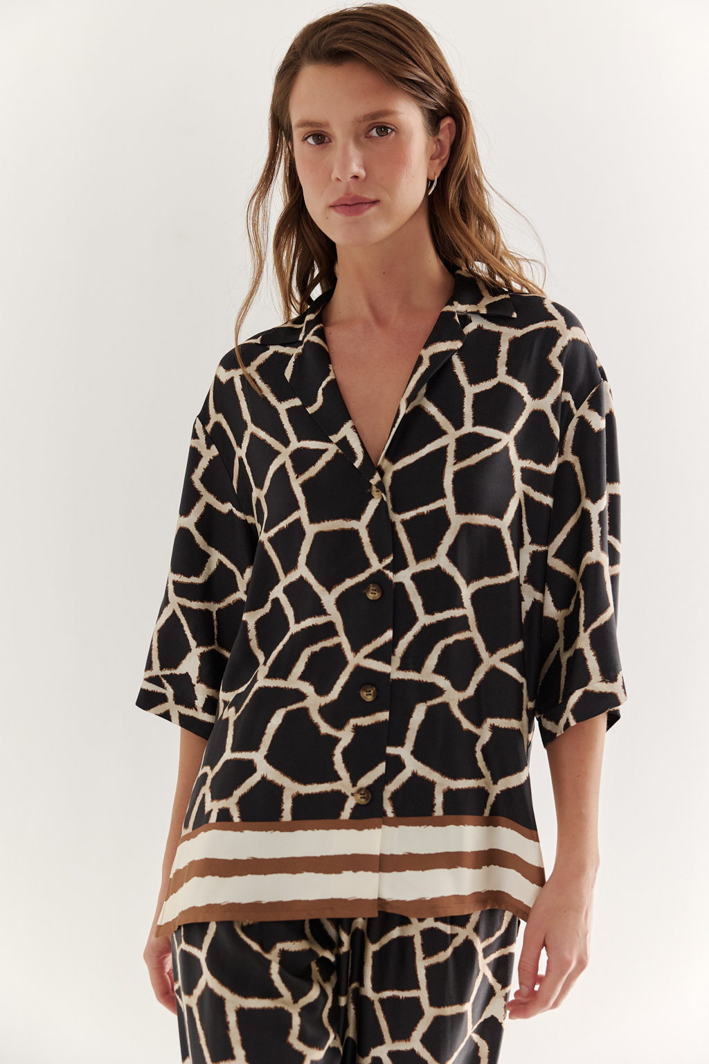 Блуза с коротким рукавом, выполненная из полированной вискозы с шелковистой текстурой, украшена эксклюзивным анималистическим принтом, разработанным дизайнерами бренда. Отложной воротник, застежка на пуговицы по переду и деликатные разрезы в боковых швах подчеркивают изысканный силуэт. Уникальный бордюр завершает принт по низу изделия, добавляя акцент. Блуза, сочетающая в себе непринужденный стиль и комфорт, идеально подходит в качестве второго слоя к пижамным брюкам из той же коллекции, создавая гармоничный и расслабленный образ.