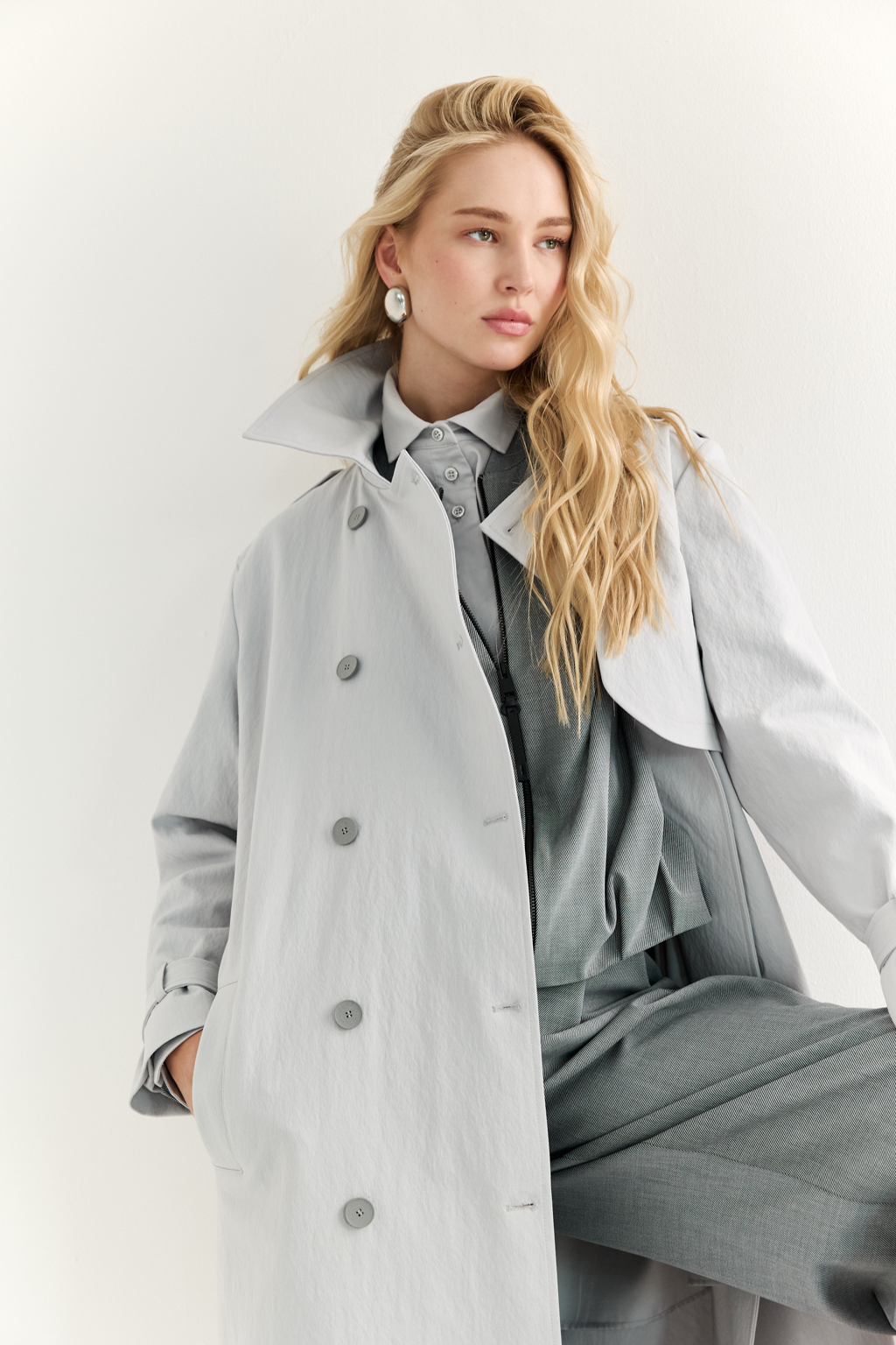 Плащ двубортный прямого силуэта длиной макси с расширенной линией плеча и отлётными кокетками по полочке и спинке. Приталивается завязывающимся поясом.