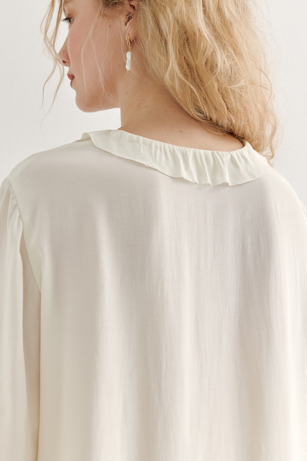 Эта романтичная блуза выполнена из вискозного крепа в нежном оттенке словочное масло. Горловина и рукава украшены изящными рюшами, добавляющими образу легкости и утонченности. Оригинальный разрез спереди кокетливо завязывается на тонкий шнур-рулик и фиксируется воздушной петлей на пуговицу. Прямой силуэт и рукава длиной одна вторая обеспечивают комфорт и свободу движений. Эта блуза — идеальный выбор для создания непринужденных, но элегантных городских образов.