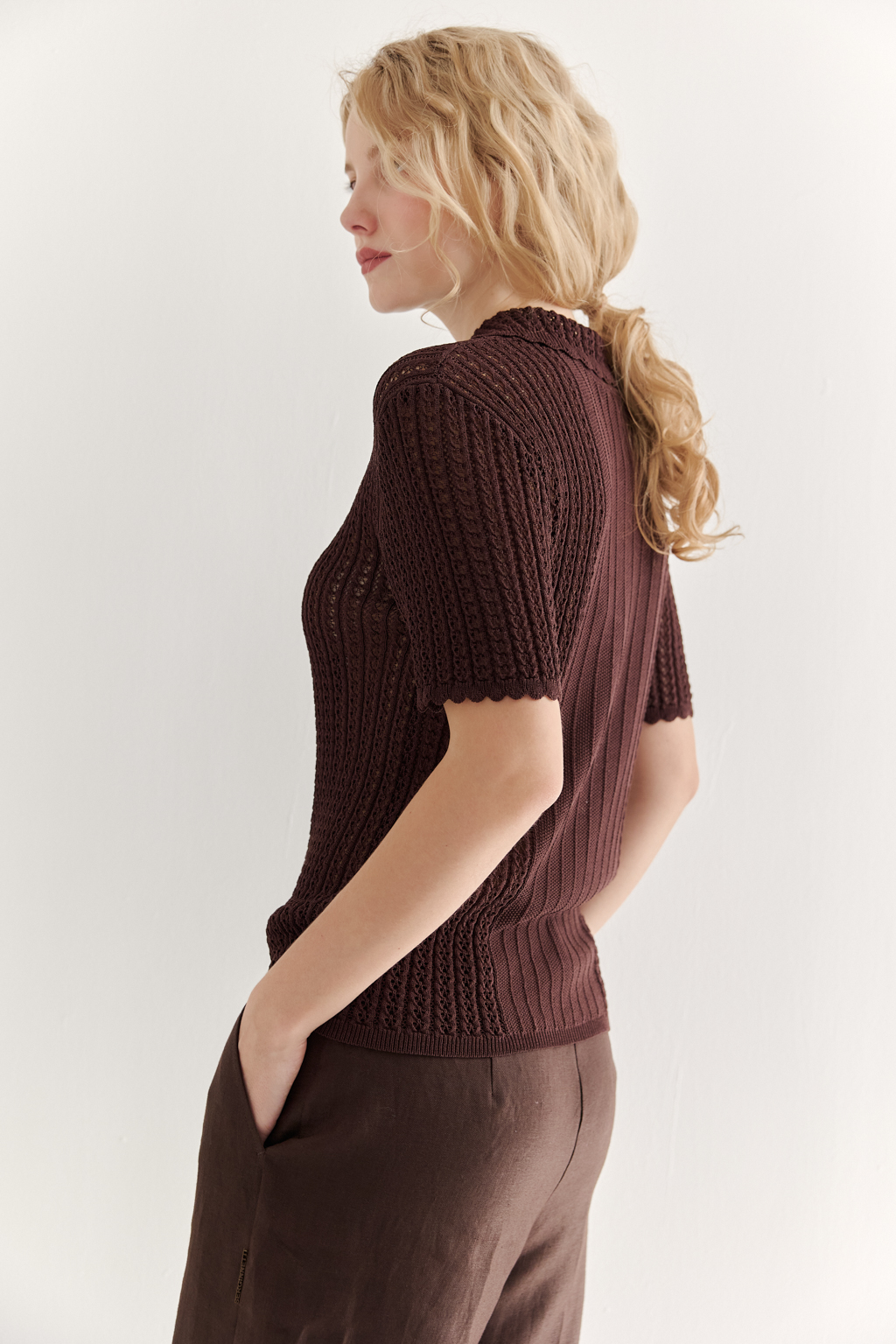 Джемпер-поло шоколадно-коричневого цвета полуприлегающего силуэта средней длины из вискозной пряжи, выполнен в комбинации полупрозрачной сетки и жаккарда, низ рукава и оторочка воротника - изящные фестоны. Рукав короткий, застежка на укороченной планке горловины на три пуговицы.