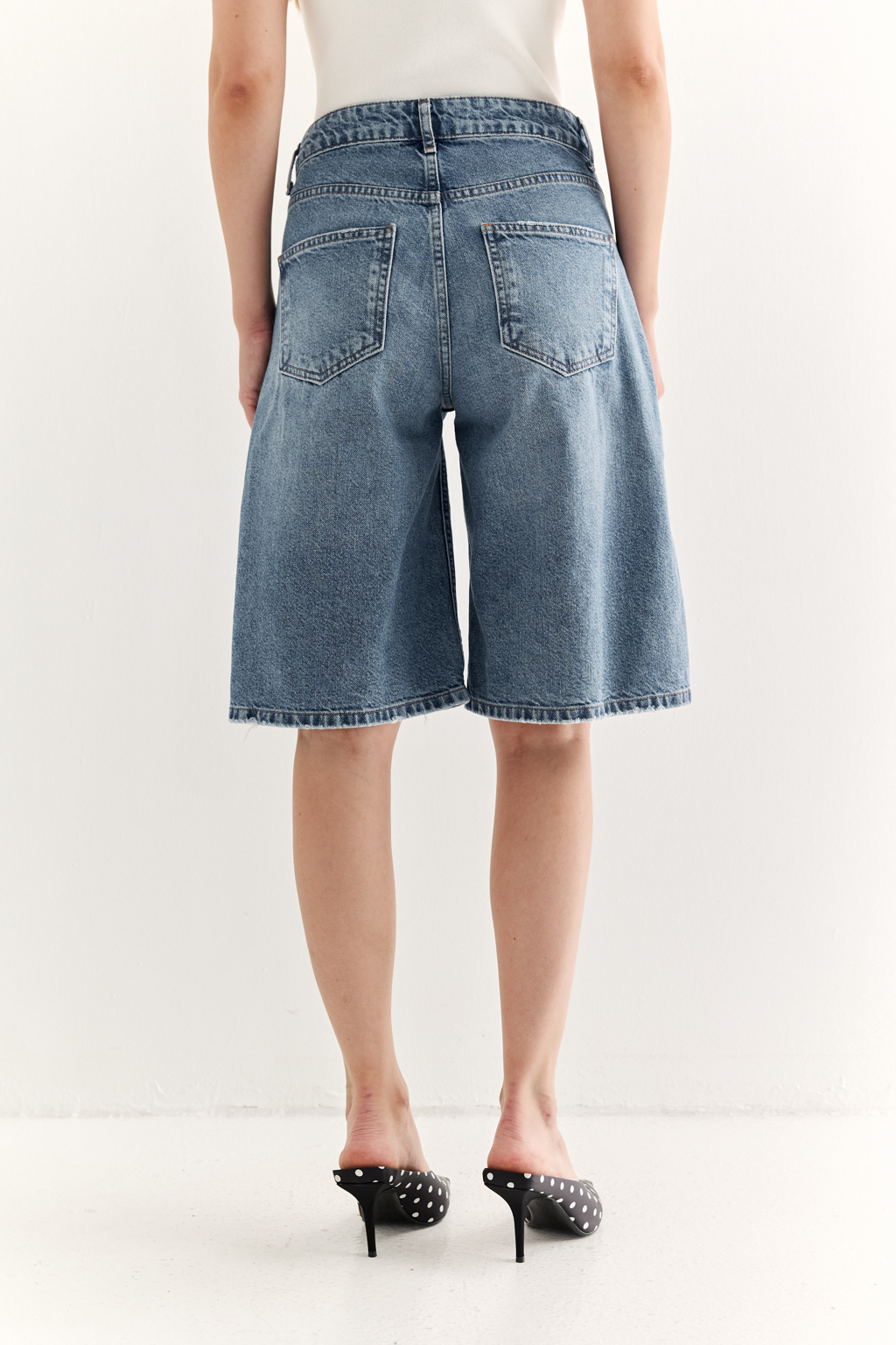 Широкие женские джинсовые шорты ниже колена из легкого денима в синем цвете. Эффект легкой потертости придаст образам расслабленности.