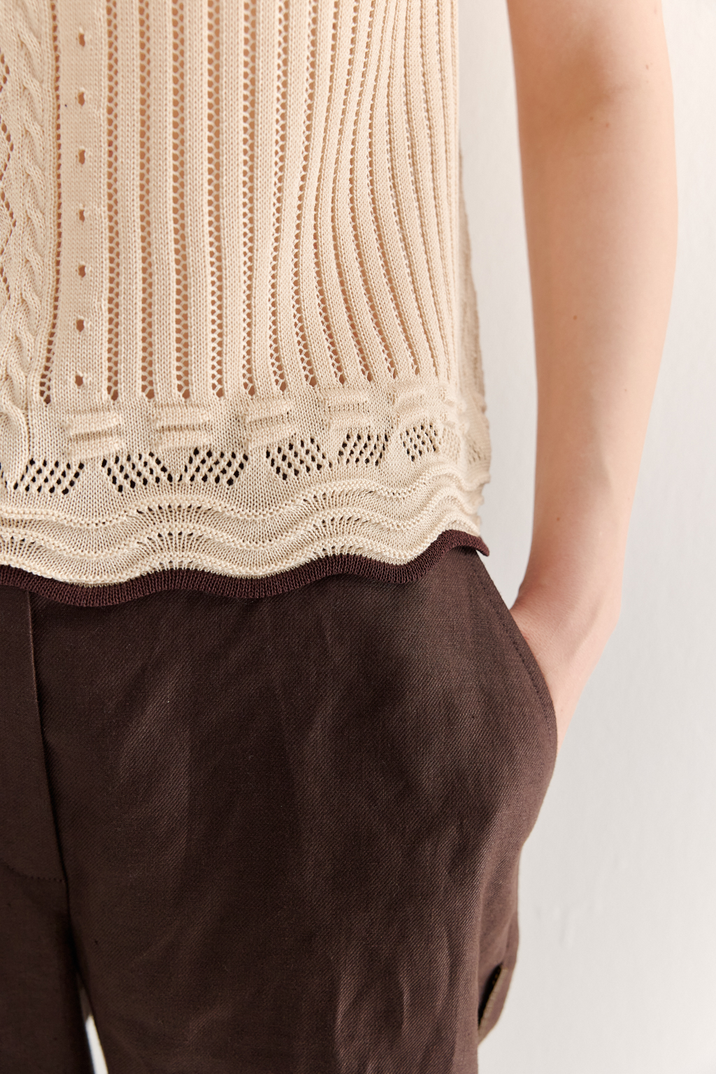 Кремовый топ в стиле пэчворк, в котором соединились четыре техники ажурной вязки, круглая горловина и деликатные рюши по пройме. Контрастная отделка коричневого цвета расположена по линиям горловины, низа и краю рюши.