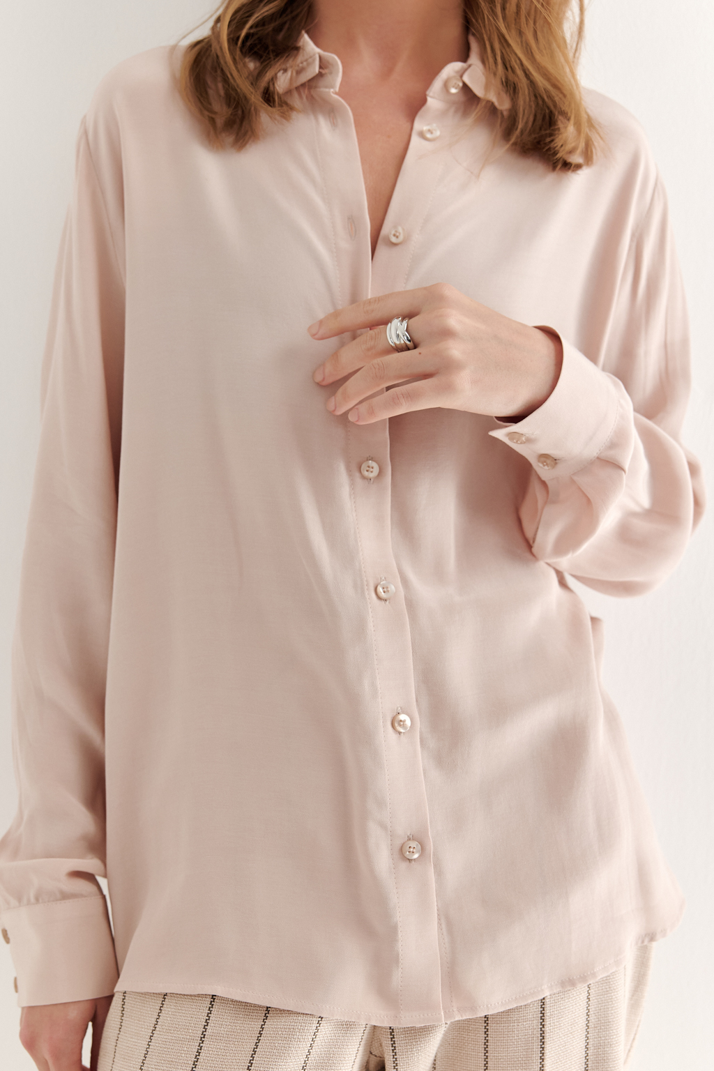 Блуза-батник в нежном пудрово-розовом оттенке станет изысканным дополнением к жакету, брюкам или верхней одежде, позволяя создавать актуальные многослойные образы. Изготовленная из вискозной ткани, она обладает превосходными тактильными качествами и напоминает дорогой шелковый креп. Классическая блузка свободного кроя с отложным воротником и стойкой, украшенной узким рюшем, имеет кокетку спинки, планку для застежки и втачной прямой рукав с манжетой на пуговицах.