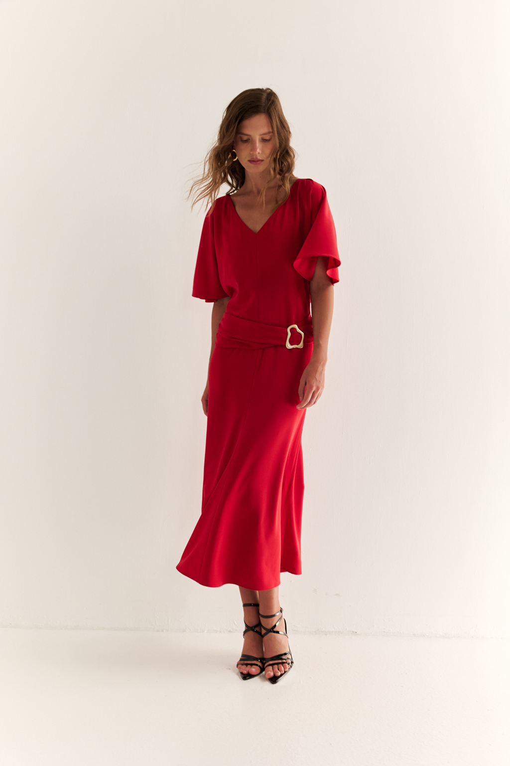 Струящееся платье свободного кроя с цельнокроеными рукавами и открытой горловиной с V-образным вырезом горловины. Модель с декоративной пряжкой на притачном поясе со сборкой по бокам. Выполнено из эластичной плательной ткани. Полиэстер придает ткани устойчивость к сминанию и хорошо держит форму. Что позволяет изделию сохранять опрятный вид в течении дня.  Спандекс добавляет эластичность, обеспечивая идеальную посадку по фигуре. Преимущества ткани: новое современное качество с мягким блеском и благородной фактурой. Ткань легкая, приятна к телу, красиво драпируется при движении. Насыщенный красный цвет делает платье эффектным.