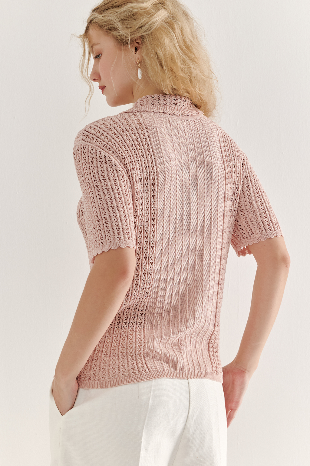 Джемпер-поло нежно-розового цвета полуприлегающего силуэта средней длины из вискозной пряжи, выполнен в комбинации полупрозрачной сетки и жаккарда, низ рукава и оторочка воротника - изящные фестоны. Рукав короткий, застежка на укороченной планке горловины на три пуговицы.