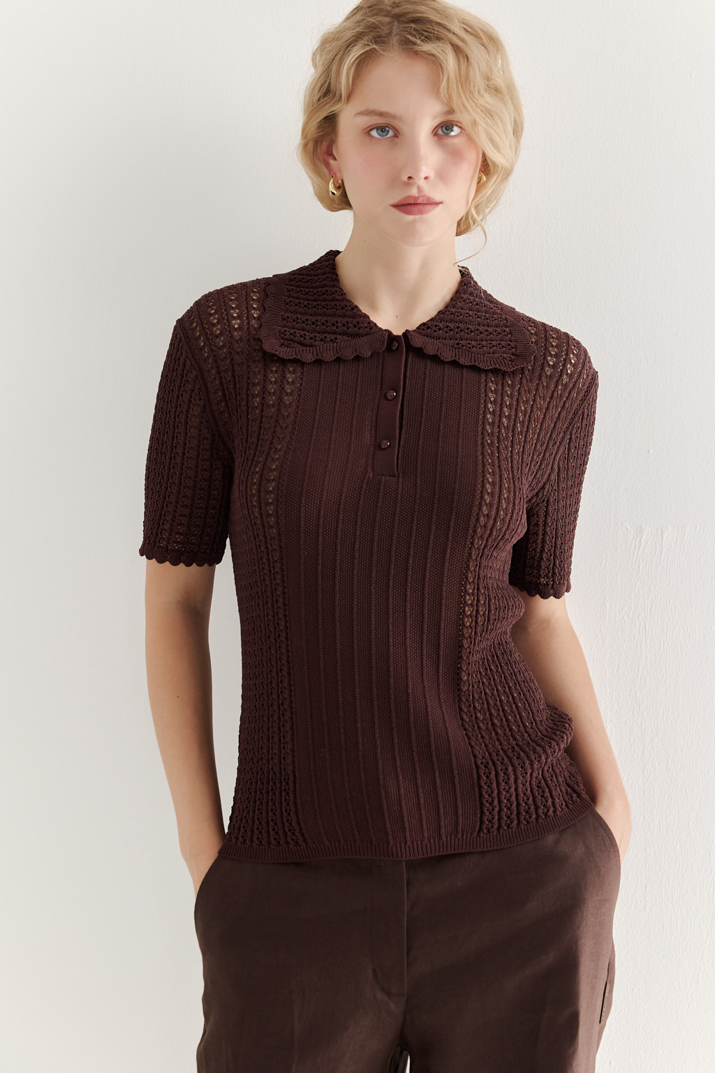 Джемпер-поло шоколадно-коричневого цвета полуприлегающего силуэта средней длины из вискозной пряжи, выполнен в комбинации полупрозрачной сетки и жаккарда, низ рукава и оторочка воротника - изящные фестоны. Рукав короткий, застежка на укороченной планке горловины на три пуговицы.