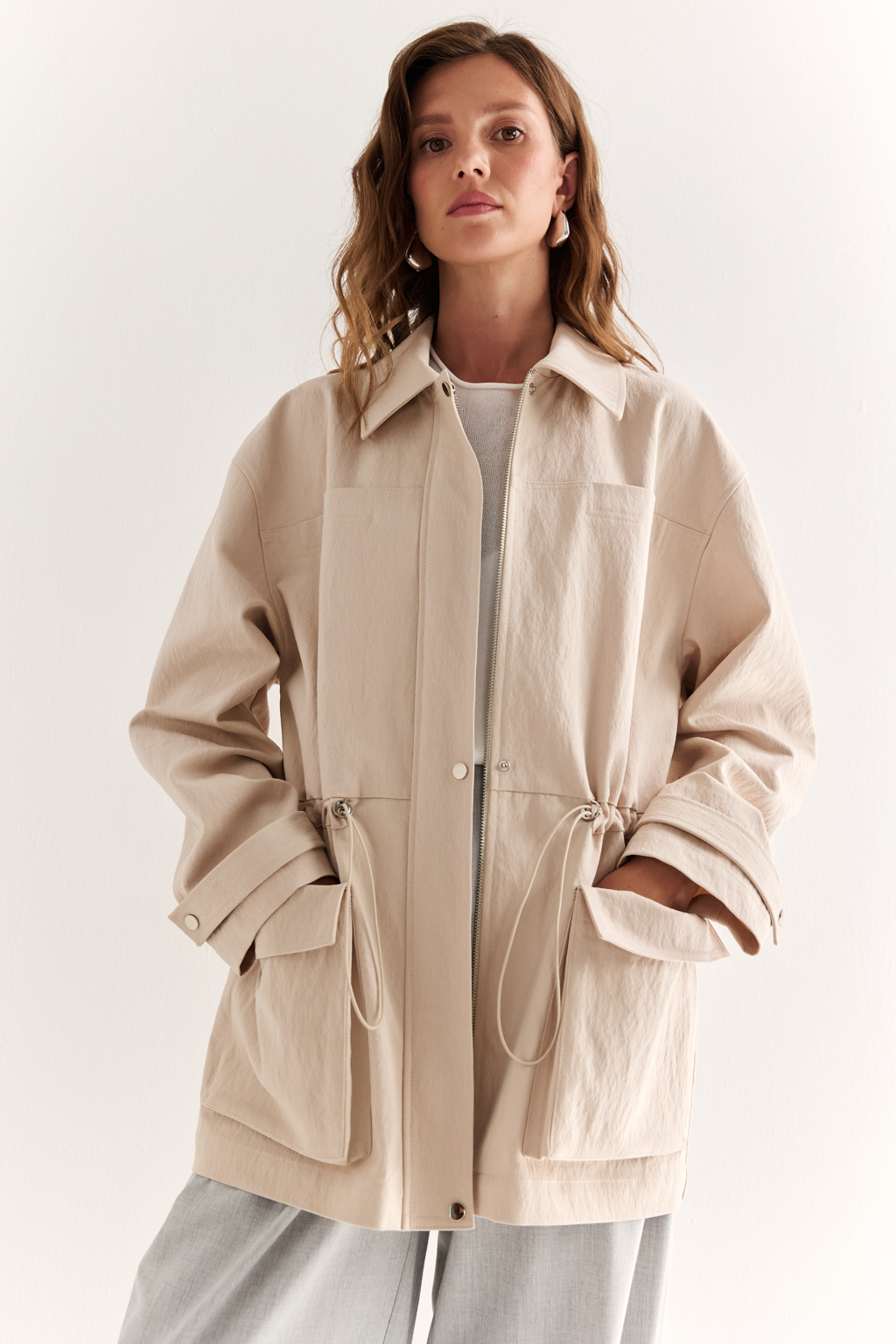 Куртка прямого силуэта длиной до бедер и с кулисой по талии. Воротник рубашечный, застежка под планкой. По полочке накладные карманы-портфели.