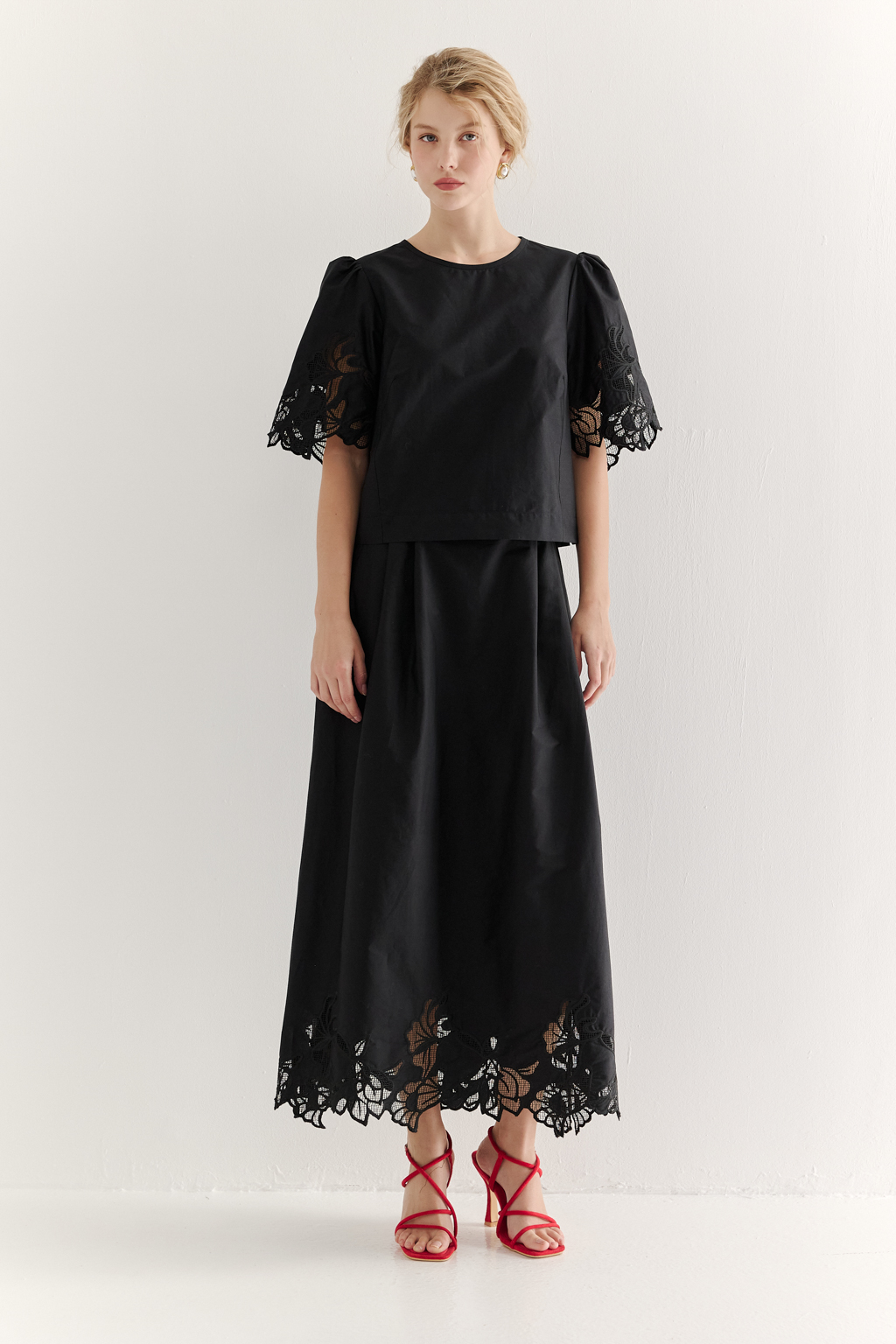 Блуза-кроп выполненная из хлопкового полотна, декорирована нежным шитьем-решелье черного цвета. Укороченный силуэт блузы дополнен широкой подгибкой по низу и элегантными разрезами в боковых швах. Горловина оформлена в виде лодочки, визуально удлиняя шею. Широкие рукава имеют сборку по окату и украшены шитьем по низу, что придает образу легкости и женственности. Молния, расположенная в среднем шве спинки, обеспечивает комфорт и удобство при носке. Идеально подойдет к юбке с шитьем-решелье белого цвета.