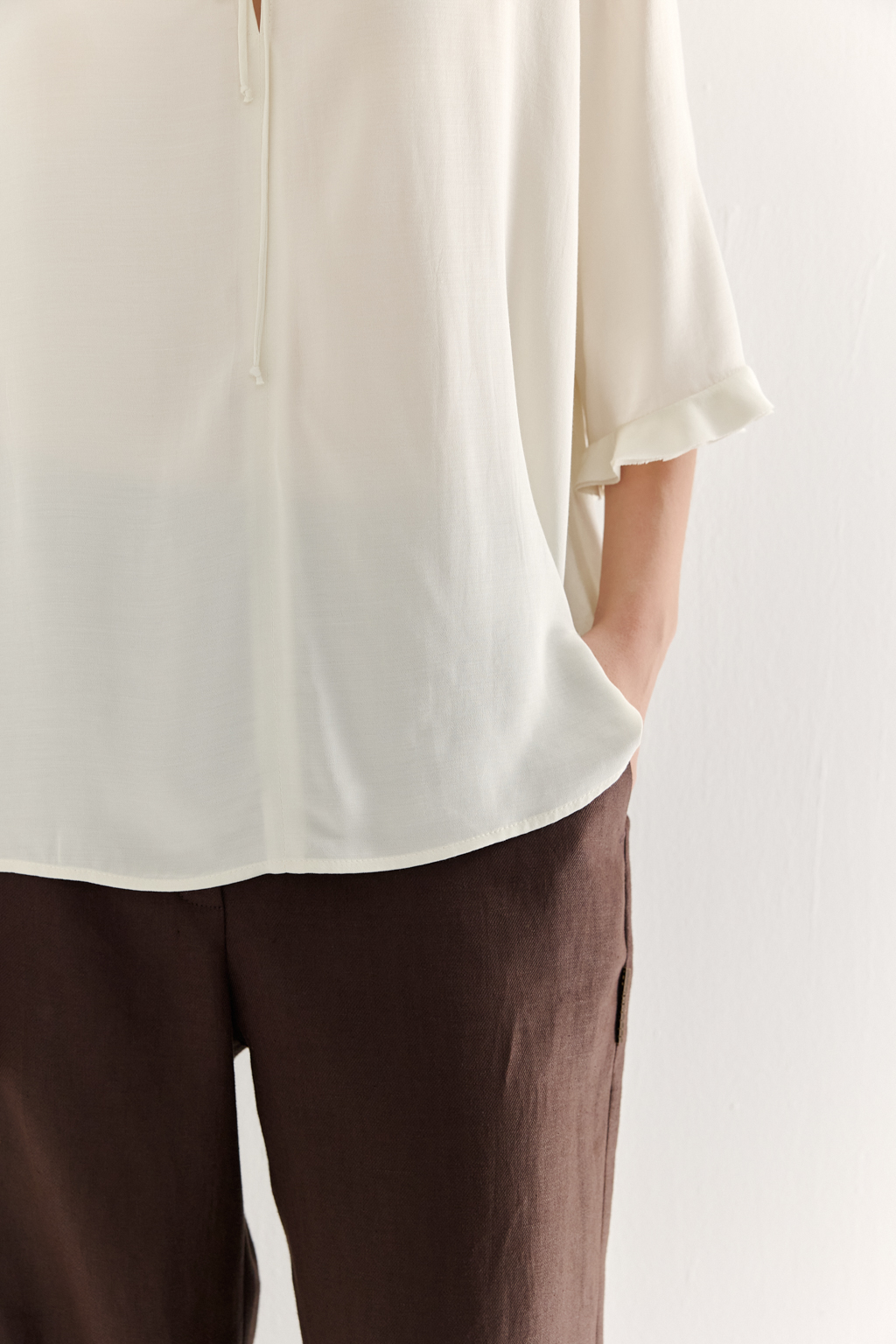 Эта романтичная блуза выполнена из вискозного крепа в нежном оттенке словочное масло. Горловина и рукава украшены изящными рюшами, добавляющими образу легкости и утонченности. Оригинальный разрез спереди кокетливо завязывается на тонкий шнур-рулик и фиксируется воздушной петлей на пуговицу. Прямой силуэт и рукава длиной одна вторая обеспечивают комфорт и свободу движений. Эта блуза — идеальный выбор для создания непринужденных, но элегантных городских образов.