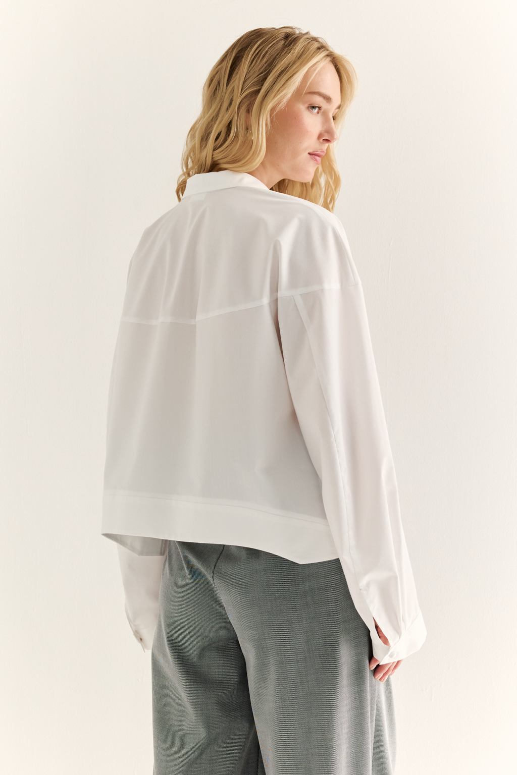 Oversize-рубашка с кокеткой: объём как способ выразить себя. Эта укороченная рубашка с удлинённой кокеткой и объёмными рукавами — модный акцент, который задаёт ритм всему образу. Мягко закруглённый низ подчёркивает талию и визуально вытягивает силуэт, а объёмный крой создаёт эффект расслабленного шика. Широкая кокетка, фактурные швы и сборка по рукавам добавляют архитектурности и свежести классической рубашке. Застёжка на пуговицы и аккуратный воротник сохраняют баланс между формальностью и актуальностью. Новая форма свободы — уверенная, воздушная, выразительная.