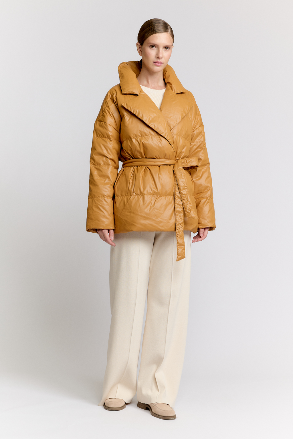 Короткий стеганый пуховик с английским воротником в горчичном цвете, застегивается на кнопки, имеет регулируемый пояс, что позволяет носить изделие в разных вариациях.