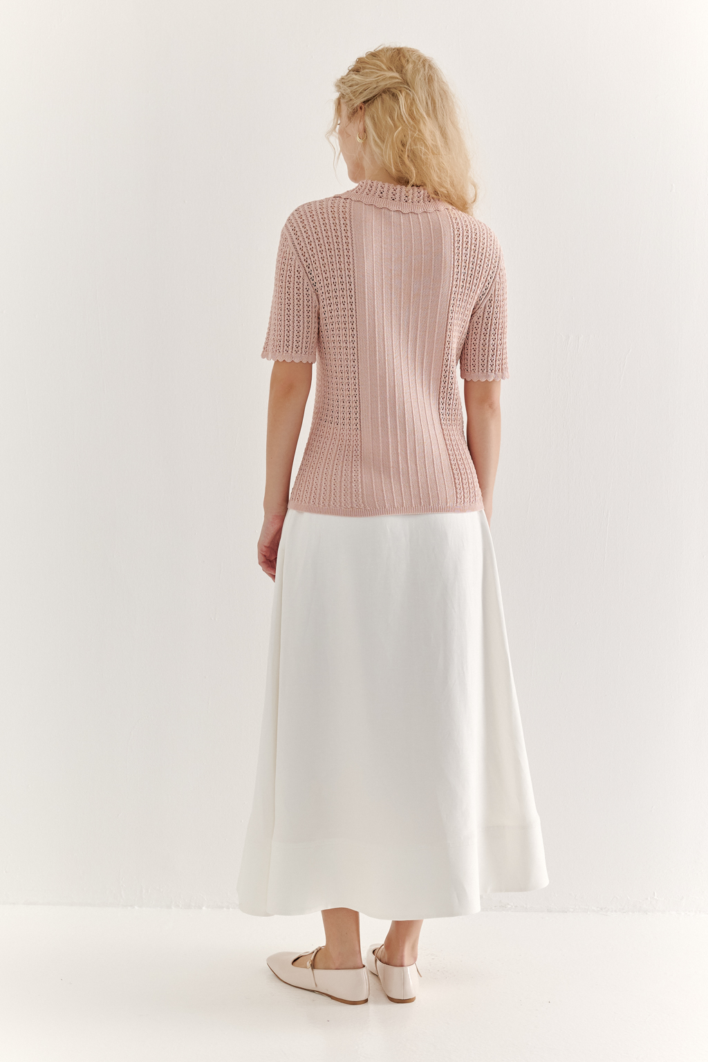 Джемпер-поло нежно-розового цвета полуприлегающего силуэта средней длины из вискозной пряжи, выполнен в комбинации полупрозрачной сетки и жаккарда, низ рукава и оторочка воротника - изящные фестоны. Рукав короткий, застежка на укороченной планке горловины на три пуговицы.