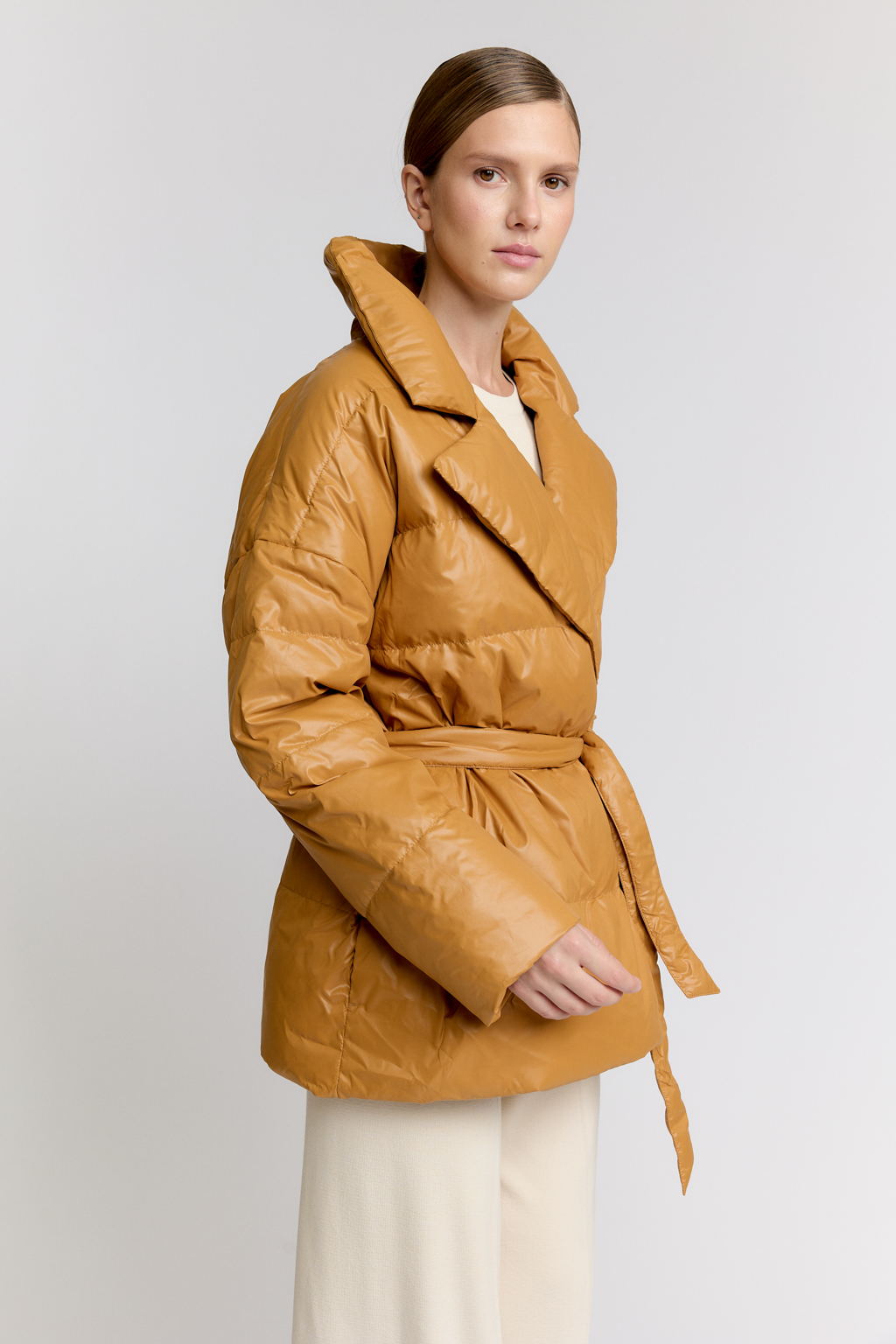 Короткий стеганый пуховик с английским воротником в горчичном цвете, застегивается на кнопки, имеет регулируемый пояс, что позволяет носить изделие в разных вариациях.
