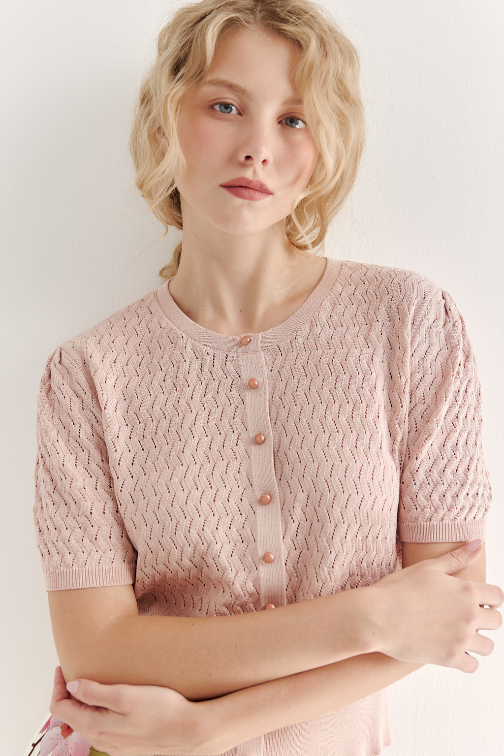 Джемпер нежно-розового цвета, связанный из тонкой тактильной пряжи, в составе которой вискоза и нейлон. В дизайне джемпера применен принцип контраста фактур, в данном случае – полупрозрачного ажура и ластика. Круглая горловина и планка с застежкой на 9 пуговиц-жемчужин, рукав длиной одна вторая.