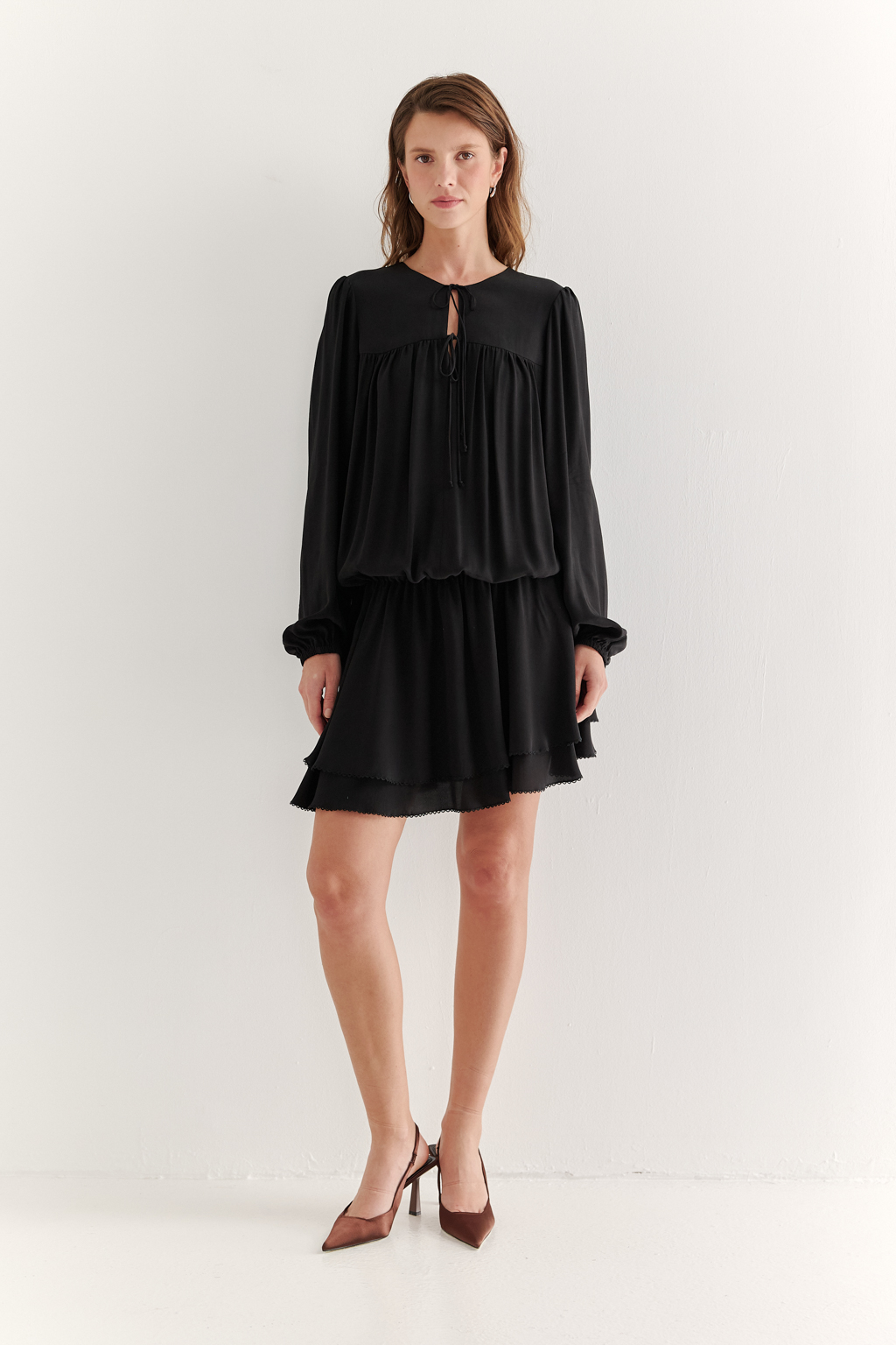 Платье, из струящейся креповой вискозы в черном цвете, представляет собой воплощение модных тенденций, умело играя с объемами с акцентом на заниженную линию талии. Это короткое, воздушное и исполненное романтики платье, сознательно избегающее вычурных деталей, является идеальным решением для создания актуального летнего городского образа. Объем платья образуется благодаря изящным сборкам, расположенным по кокеткам переда и спинки. Отрезная юбка, расширяющаяся к низу, украшена деликатной декоративной строчкой-вышивкой в виде фестонов. Линия отреза юбки оформлена эластичной тесьмой-стрейч, что дает возможность регулировать длину. Платье гармонично сочетается с рубашками или жакетами, предоставляя свободу для экспериментов со стилем. При желании можно усложнить образ образа с помощью леггинсов и также подчеркнуть талию элегантным кожаным ремнем.