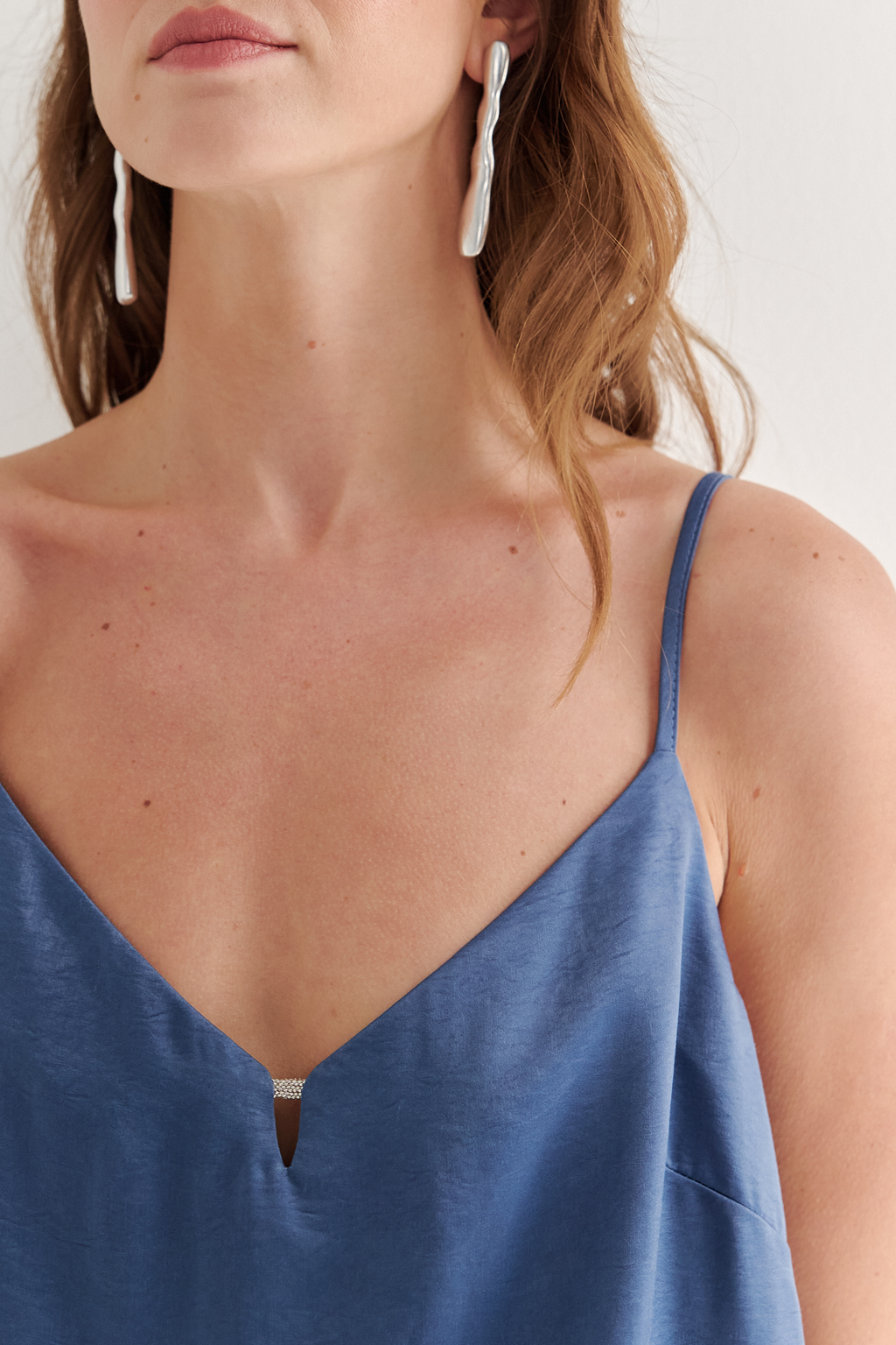 Топ из струящегося атласа с крэш эффектом в цвете деним. Топ на регулируемых бретелях свободного кроя с декором на линии декольте.