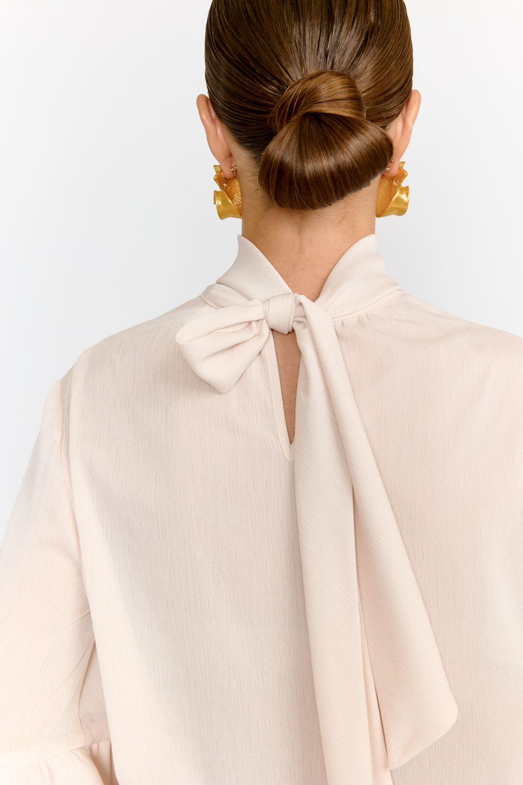 Блуза свободного кроя с легким расширением к низу с воланами и воротником-стойкой, переходящим в ленты, которые можно завязать в бант либо просто перекинуть через плечи. Выполнена из легкой полупрозрачной ткани. Крэш-шифон -легкий, дышащий материал, создающий эффект невесомости. Полиэстеровые волокна в составе обеспечивают   неприхотливость в уходе и устойчивость к механическим повреждениям. Нежный цвет экрю позволяет легко вписать блузу в гардероб, для создания как праздничных образов, так и повседневных.