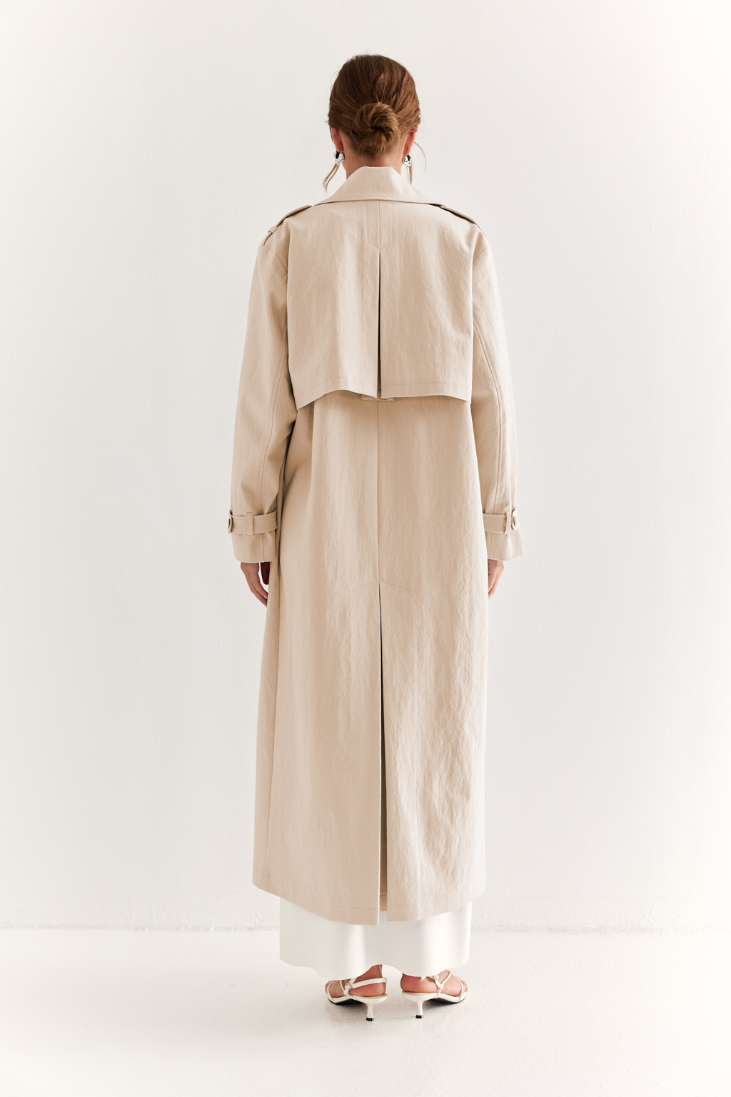 Плащ двубортный прямого силуэта длиной макси с расширенной линией плеча и отлётными кокетками по полочке и спинке. Приталивается завязывающимся поясом.