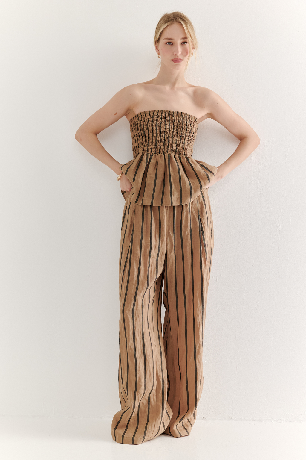 Топ-бандо из эластичных стрейч-нитей, выполненный из платьевой ткани с полской. Состав ткани представляет собой гармоничное сочетание натуральных волокон крапивы и хлопка, обработанных методом растительного окрашивания (natural dye), что обеспечивает экологичность и мягкость материала. Топ состоит из двух основных частей: верхней присборенной бандо-секции и нижней части топа. Поддержка обеспечивается съемными бретелями, которые позволяют варьировать стиль ношения.