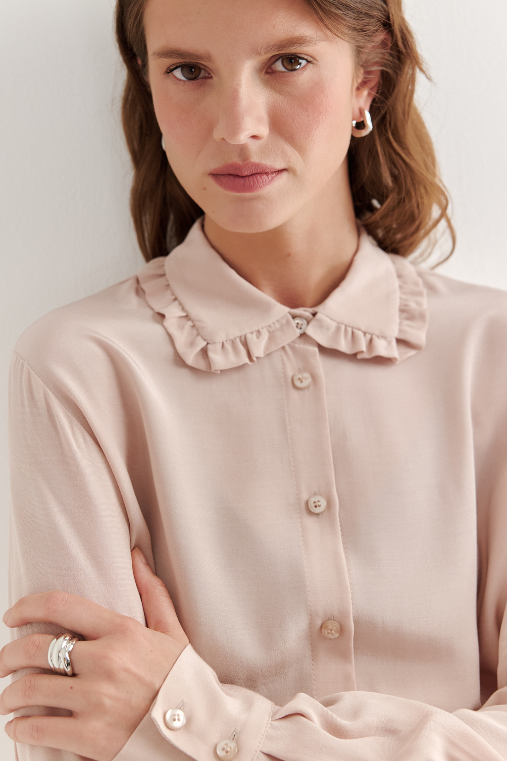 Блуза-батник в нежном пудрово-розовом оттенке станет изысканным дополнением к жакету, брюкам или верхней одежде, позволяя создавать актуальные многослойные образы. Изготовленная из вискозной ткани, она обладает превосходными тактильными качествами и напоминает дорогой шелковый креп. Классическая блузка свободного кроя с отложным воротником и стойкой, украшенной узким рюшем, имеет кокетку спинки, планку для застежки и втачной прямой рукав с манжетой на пуговицах.