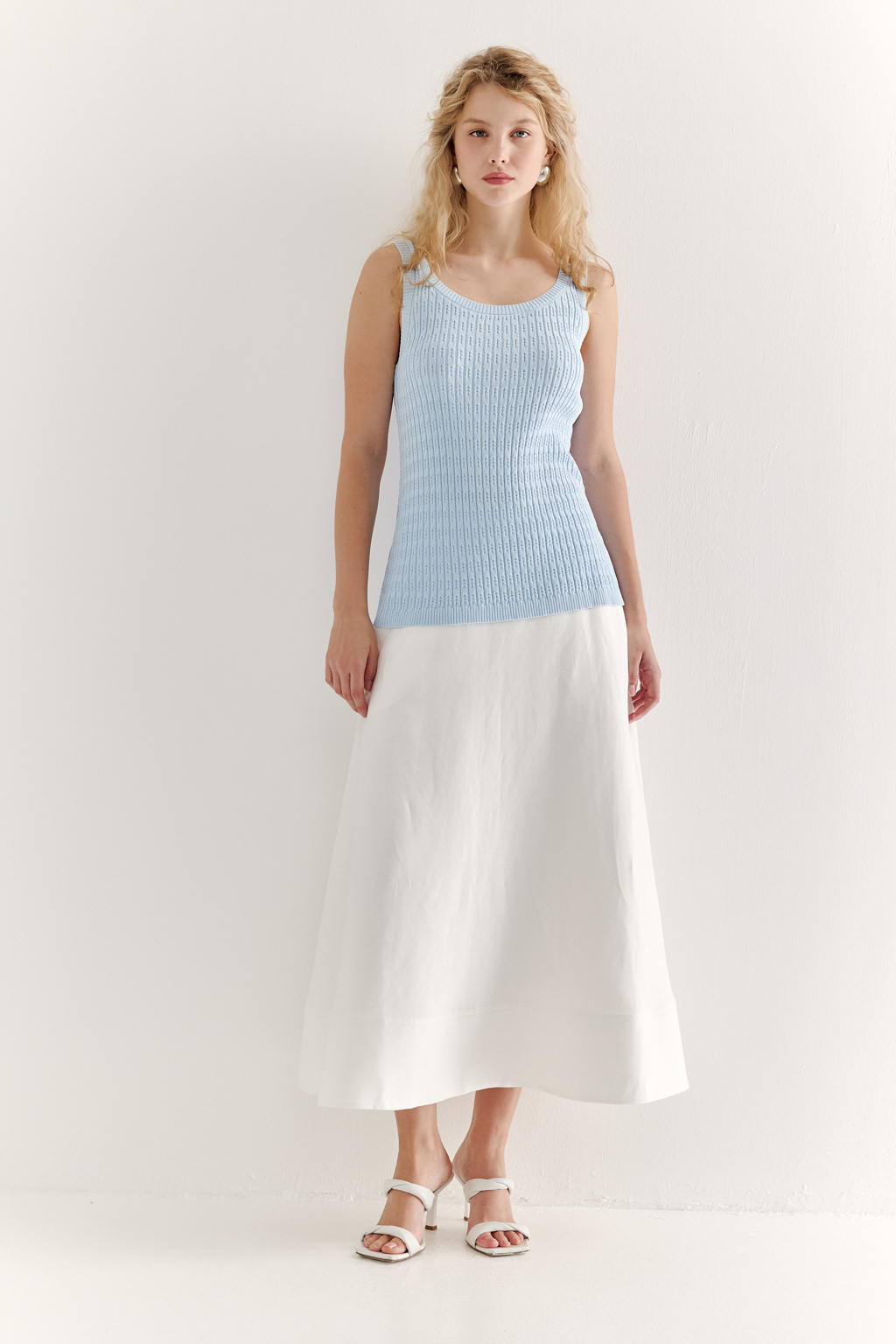 Фактурный топ-майка прилегающего силуэта из вискозной пряжи связана косами, проймы и горловина отделаны вязанными кантами. Цвет – голубой.