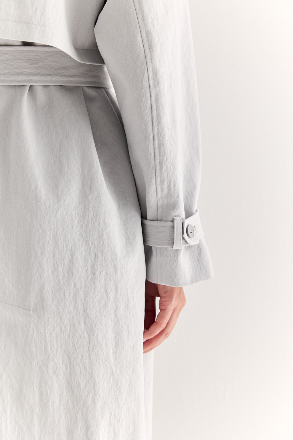 Плащ двубортный прямого силуэта длиной макси с расширенной линией плеча и отлётными кокетками по полочке и спинке. Приталивается завязывающимся поясом.