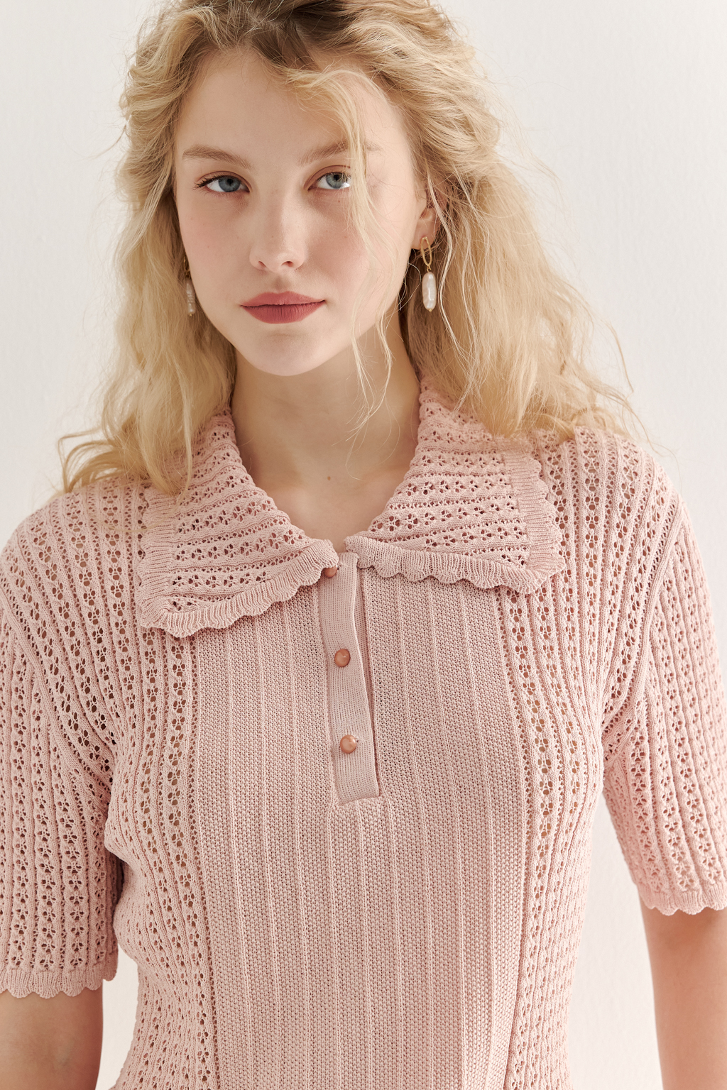 Джемпер-поло нежно-розового цвета полуприлегающего силуэта средней длины из вискозной пряжи, выполнен в комбинации полупрозрачной сетки и жаккарда, низ рукава и оторочка воротника - изящные фестоны. Рукав короткий, застежка на укороченной планке горловины на три пуговицы.