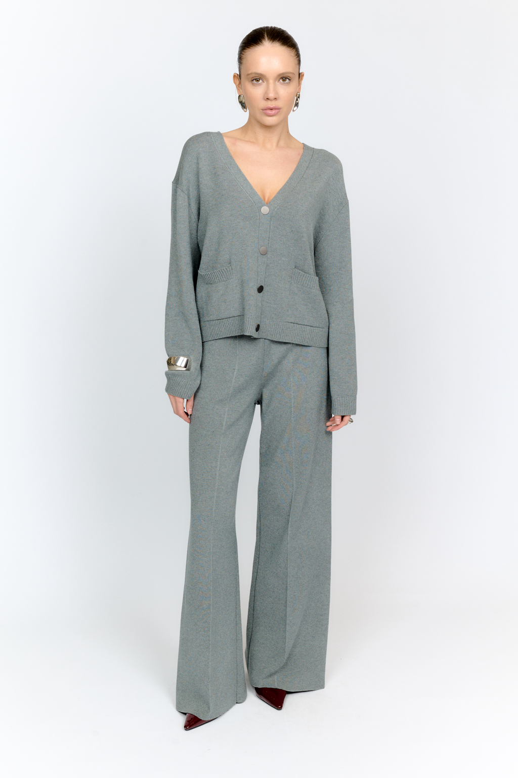 Трикотажный кардиган в сером цвете с V-образным вырезом горловины, на пуговицах, со втачным рукавом, двумя накладными карманами на полочке. Можно использовать в качестве альтернативы жакетам и носить вторым слоем в расстегнутом виде на более тонкие верха.