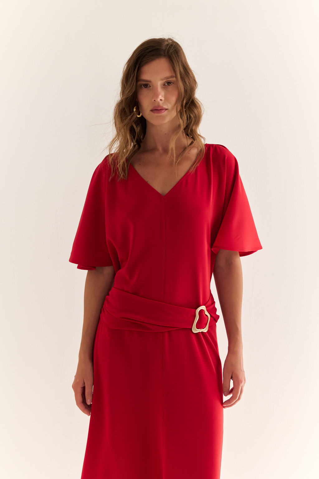 Струящееся платье свободного кроя с цельнокроеными рукавами и открытой горловиной с V-образным вырезом горловины. Модель с декоративной пряжкой на притачном поясе со сборкой по бокам. Выполнено из эластичной плательной ткани. Полиэстер придает ткани устойчивость к сминанию и хорошо держит форму. Что позволяет изделию сохранять опрятный вид в течении дня.  Спандекс добавляет эластичность, обеспечивая идеальную посадку по фигуре. Преимущества ткани: новое современное качество с мягким блеском и благородной фактурой. Ткань легкая, приятна к телу, красиво драпируется при движении. Насыщенный красный цвет делает платье эффектным.