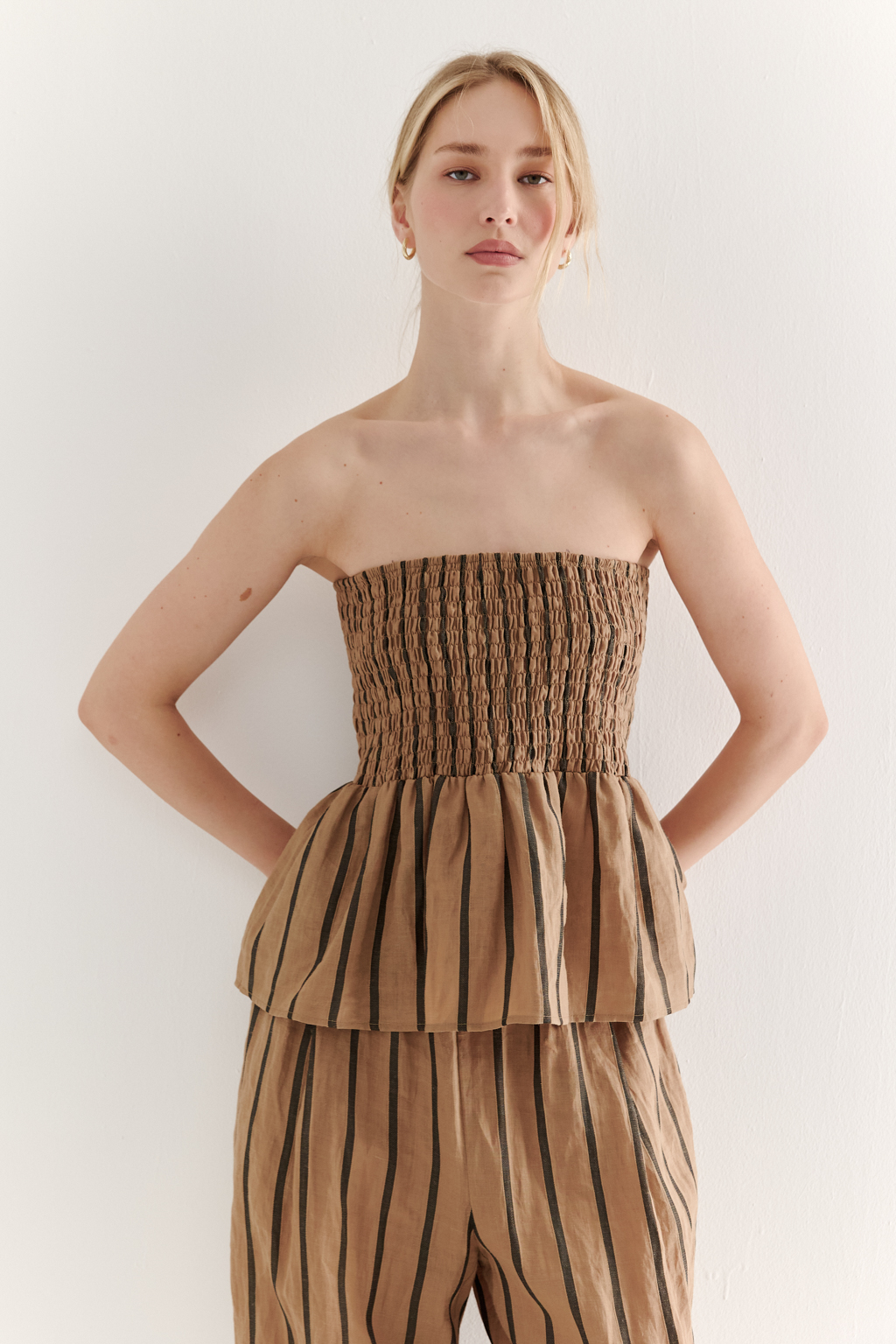 Топ-бандо из эластичных стрейч-нитей, выполненный из платьевой ткани с полской. Состав ткани представляет собой гармоничное сочетание натуральных волокон крапивы и хлопка, обработанных методом растительного окрашивания (natural dye), что обеспечивает экологичность и мягкость материала. Топ состоит из двух основных частей: верхней присборенной бандо-секции и нижней части топа. Поддержка обеспечивается съемными бретелями, которые позволяют варьировать стиль ношения.