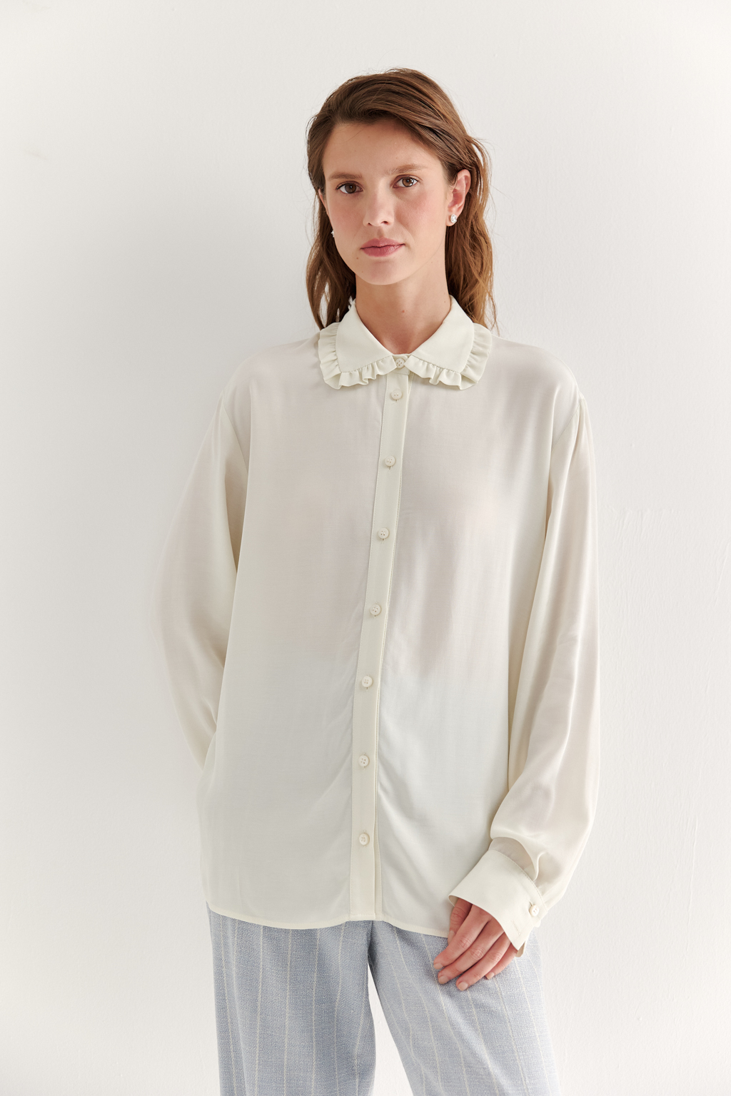 Блуза-батник в нежном оттенке сливочное масло станет изысканным дополнением к жакету, брюкам или верхней одежде, позволяя создавать актуальные многослойные образы. Изготовленная из вискозной ткани, она обладает превосходными тактильными качествами и напоминает дорогой шелковый креп. Классическая блузка свободного кроя с отложным воротником и стойкой, украшенной узким рюшем, имеет планку для застежки и втачной прямой рукав с манжетой на пуговицах.