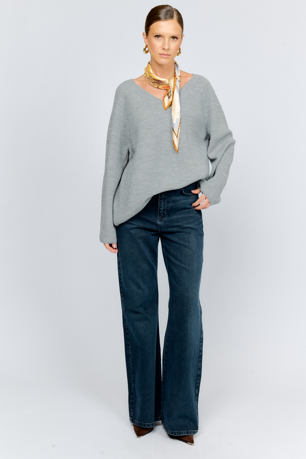 Трикотажный джемпер серого цвета свободного силуэта с V-образным вырезом горловины и рукавами реглан из шерстяной смесовой пряжи станет центром комфортных осенних образов.