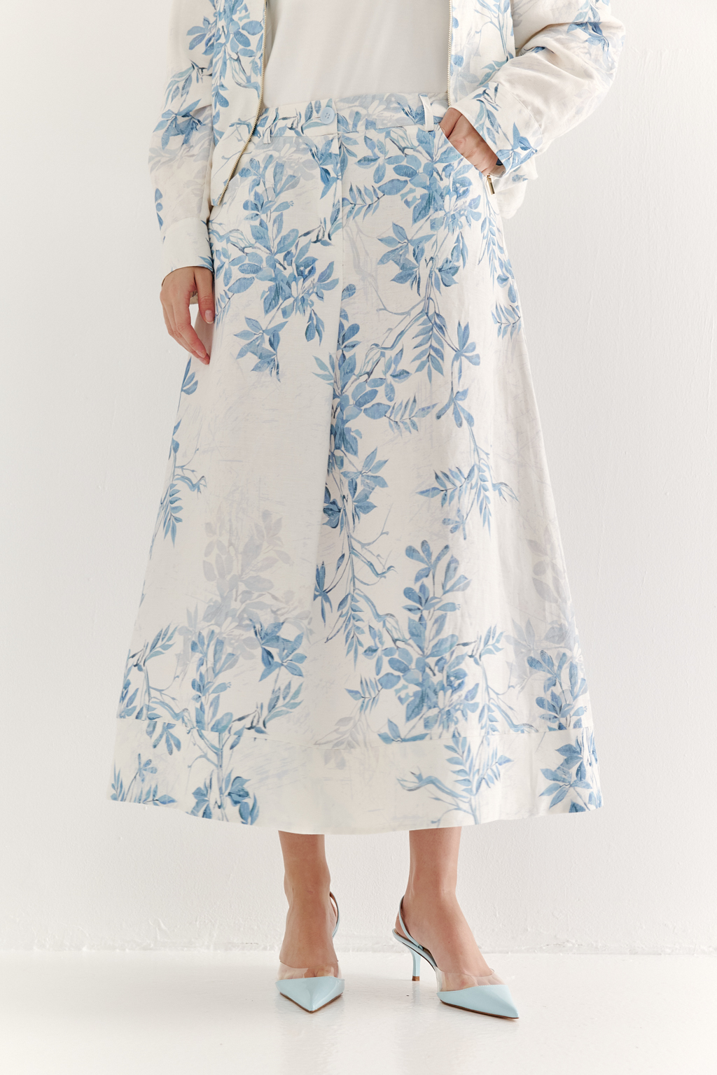 Юбка А-силуэта выполнена из ткани, в составе которой лен и вискоза. Классические детали, такие как пояс, шлевки, гульфик, кокетка спинки и отстроченные швы, представляют собой традиционное решение для джинсовых коллекций. Изюминкой модели является глубокая складка по переднему шву, обеспечивающая дополнительный комфорт и свободу движений. Главный акцент – принт в стиле знаменитого одноцветного Туаль де Жуи, где диагональная композиция из листьев и цветов выполнена в голубом цвете.