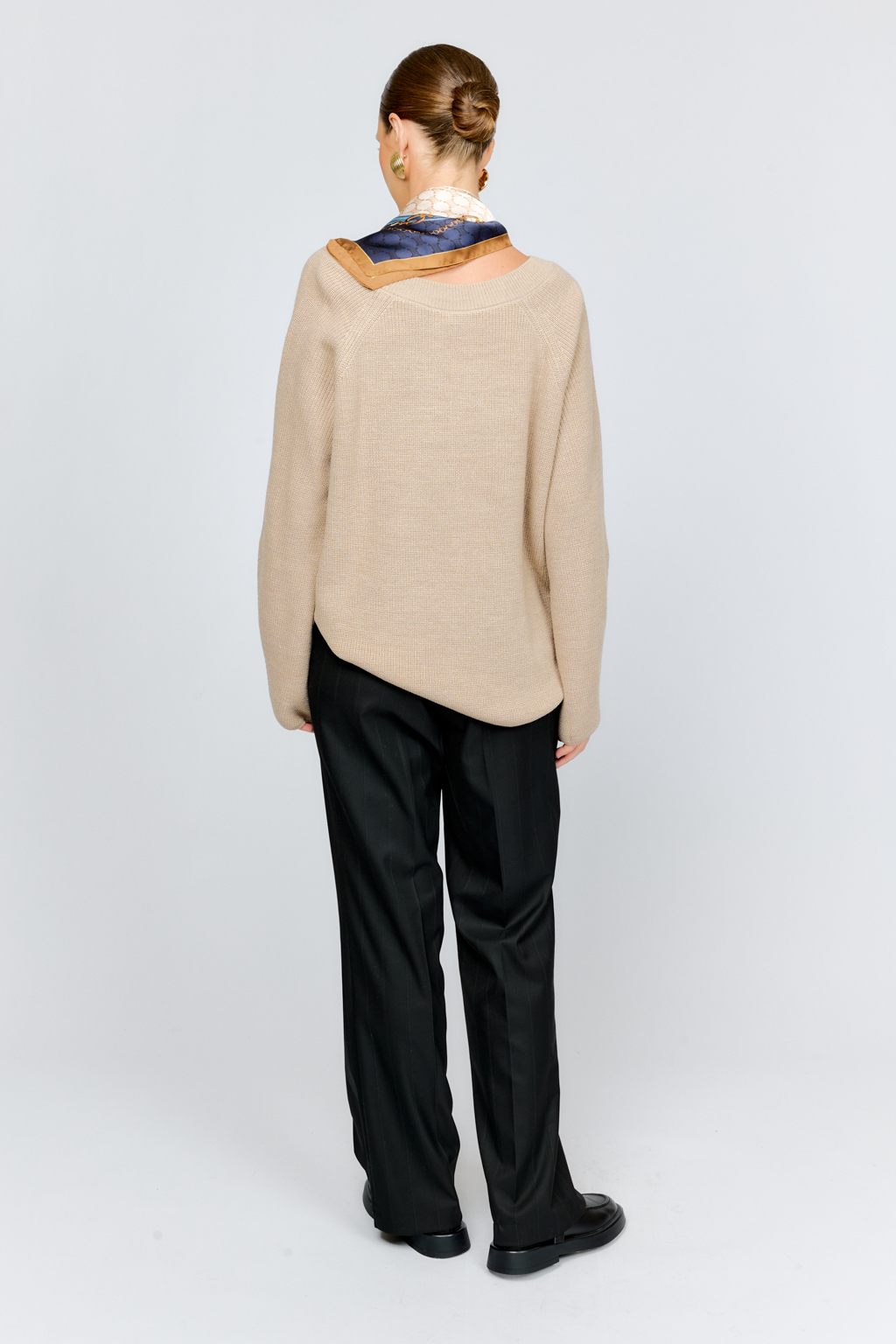 Трикотажный джемпер бежевого цвета свободного силуэта с V-образным вырезом горловины и рукавами реглан из шерстяной смесовой пряжи станет центром комфортных осенних образов.