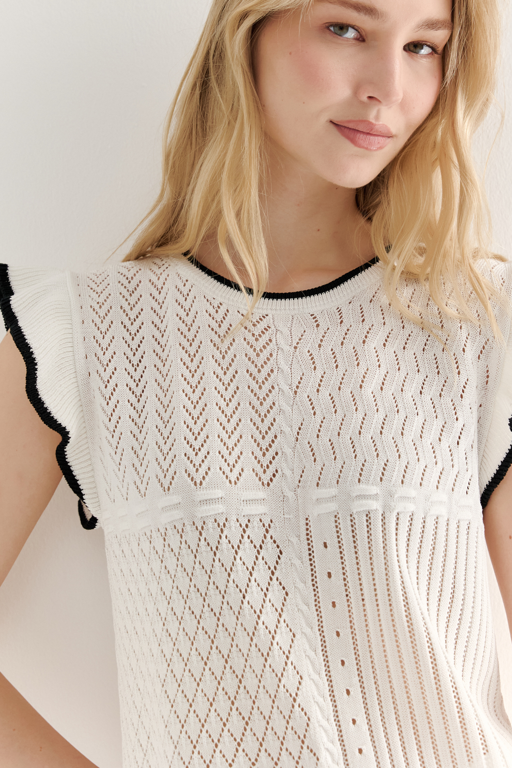 Белый топ, в котором соединились четыре техники ажурной вязки, круглая горловина и деликатные рюши по пройме. Контрастная отделка расположена по линиям горловины, низа и краю рюши.