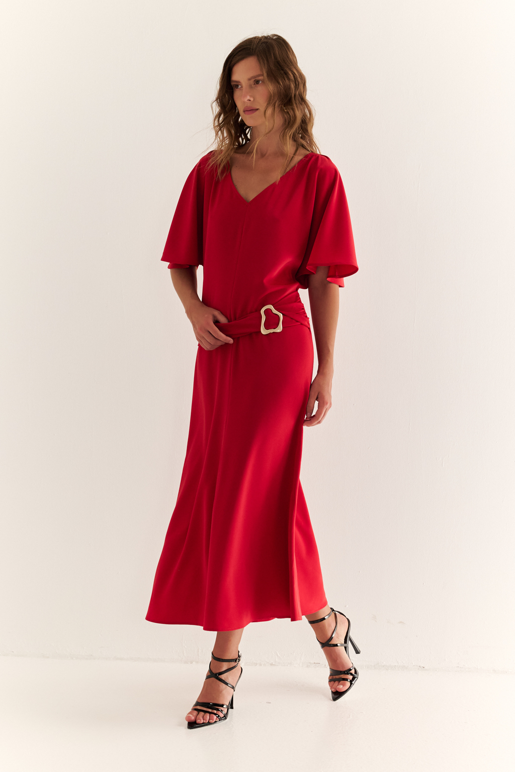 Струящееся платье свободного кроя с цельнокроеными рукавами и открытой горловиной с V-образным вырезом горловины. Модель с декоративной пряжкой на притачном поясе со сборкой по бокам. Выполнено из эластичной плательной ткани. Полиэстер придает ткани устойчивость к сминанию и хорошо держит форму. Что позволяет изделию сохранять опрятный вид в течении дня.  Спандекс добавляет эластичность, обеспечивая идеальную посадку по фигуре. Преимущества ткани: новое современное качество с мягким блеском и благородной фактурой. Ткань легкая, приятна к телу, красиво драпируется при движении. Насыщенный красный цвет делает платье эффектным.