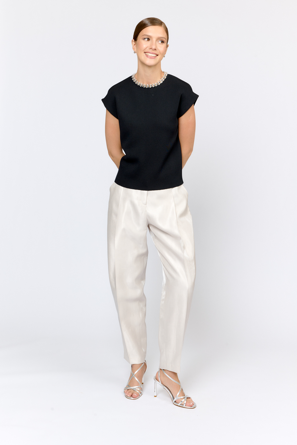 Элегантный топ  с круглой горловиной, декорированной тесьмой. Со спущенным плечом, без рукавов. Свободного силуэта. Изысканная модель из премиального  трикотажа плотной вязки в  молочном цвете. Сбалансированная комбинация вискозы и полиамида  создает комфорт при носке. Материал хорошо держит форму  и не подвержен деформации.  Лаконичный топ с декоративной тесьмой  в универсальном черном цвете  - утонченное решение для вечерних или деловых образов.